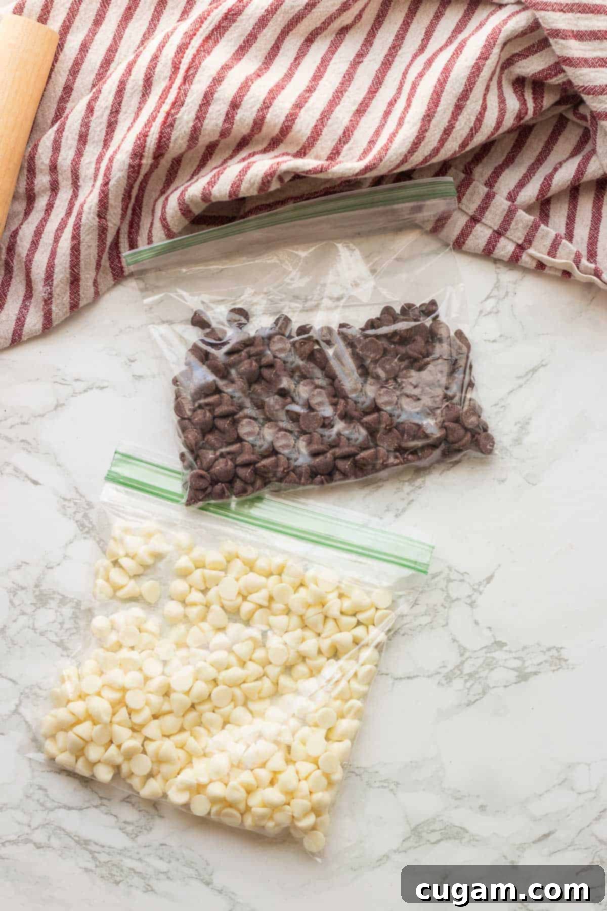 Chocolate chips and white chocolate chips in separate plastic bags on a marble countertop, ready for melting.