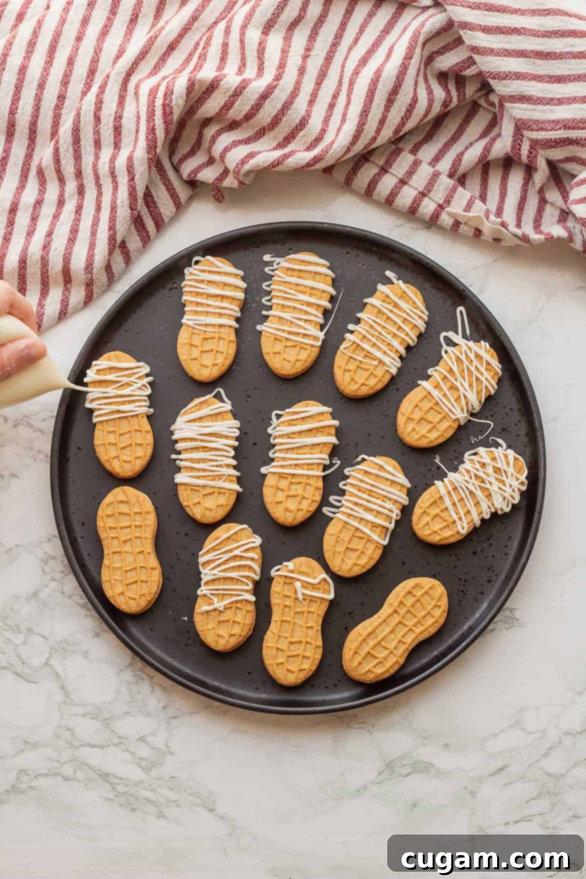 White chocolate being drizzled over Nutter Butter cookies arranged on a black plate to create mummy decorations.