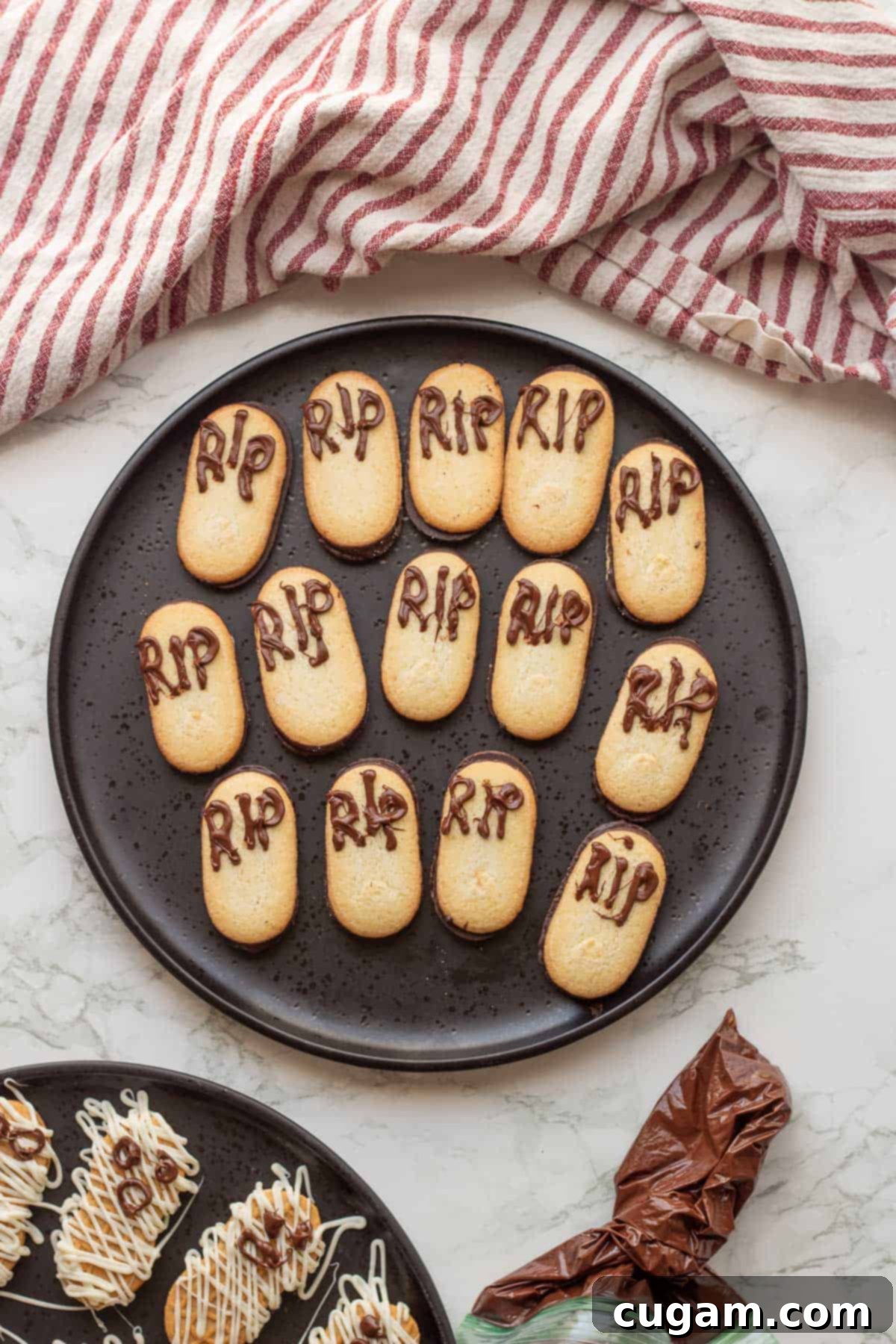 Milano cookies with 'R.I.P.' piped onto them in chocolate, resembling gravestones, on a black plate.