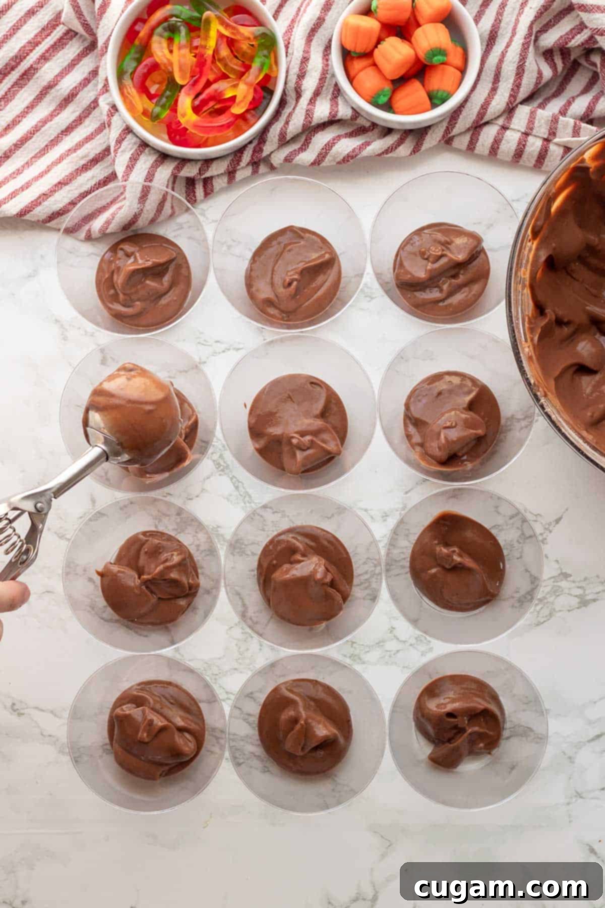 Chocolate pudding being scooped into clear plastic cups as the first layer of the dirt cups.