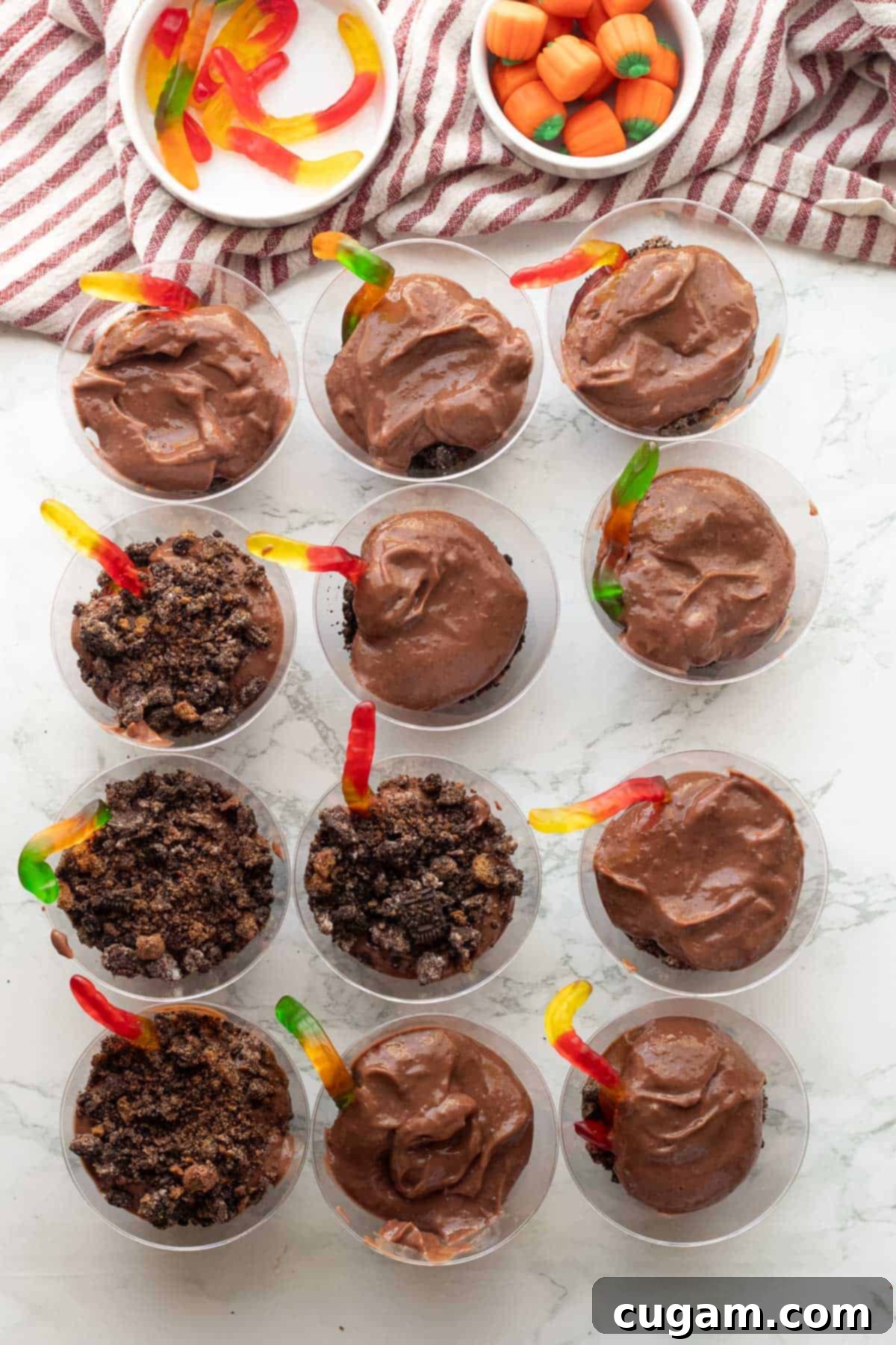 Clear plastic cups filled with layers of chocolate pudding, Oreo crumbs, and gummy worms, showcasing the dirt cup effect.