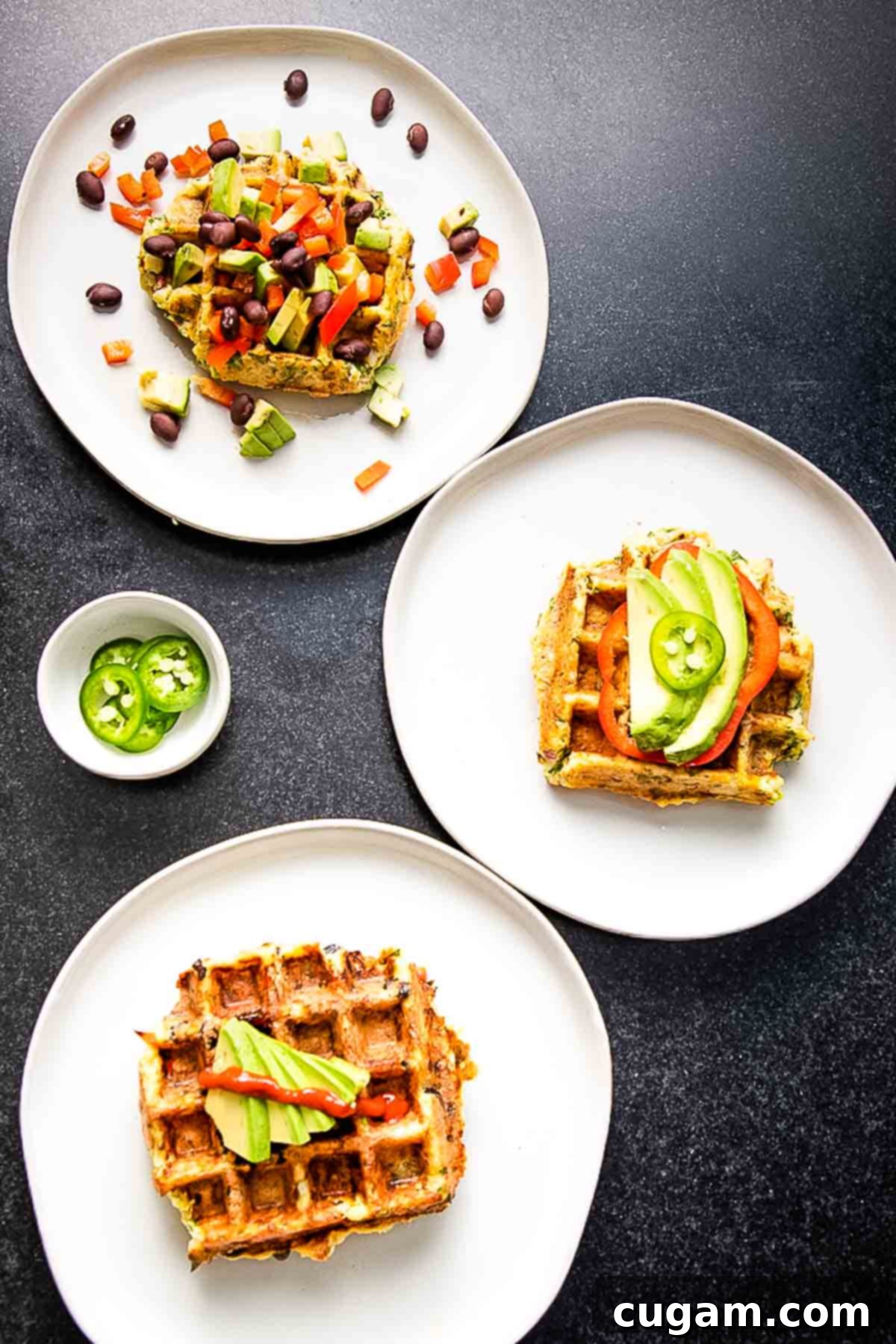 3 plates of savory waffles with assorted toppings including avocado slices, sriracha, jalapenos, black beans, chopped bell peppers.