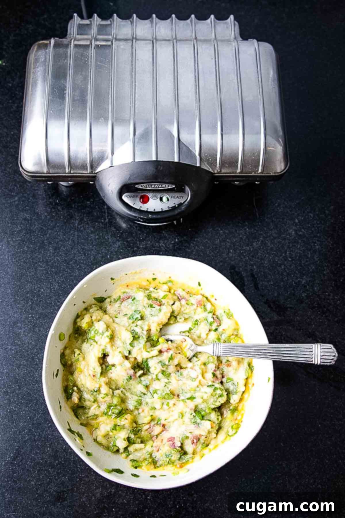 Closed waffle iron with a bowl of potato waffle batter.