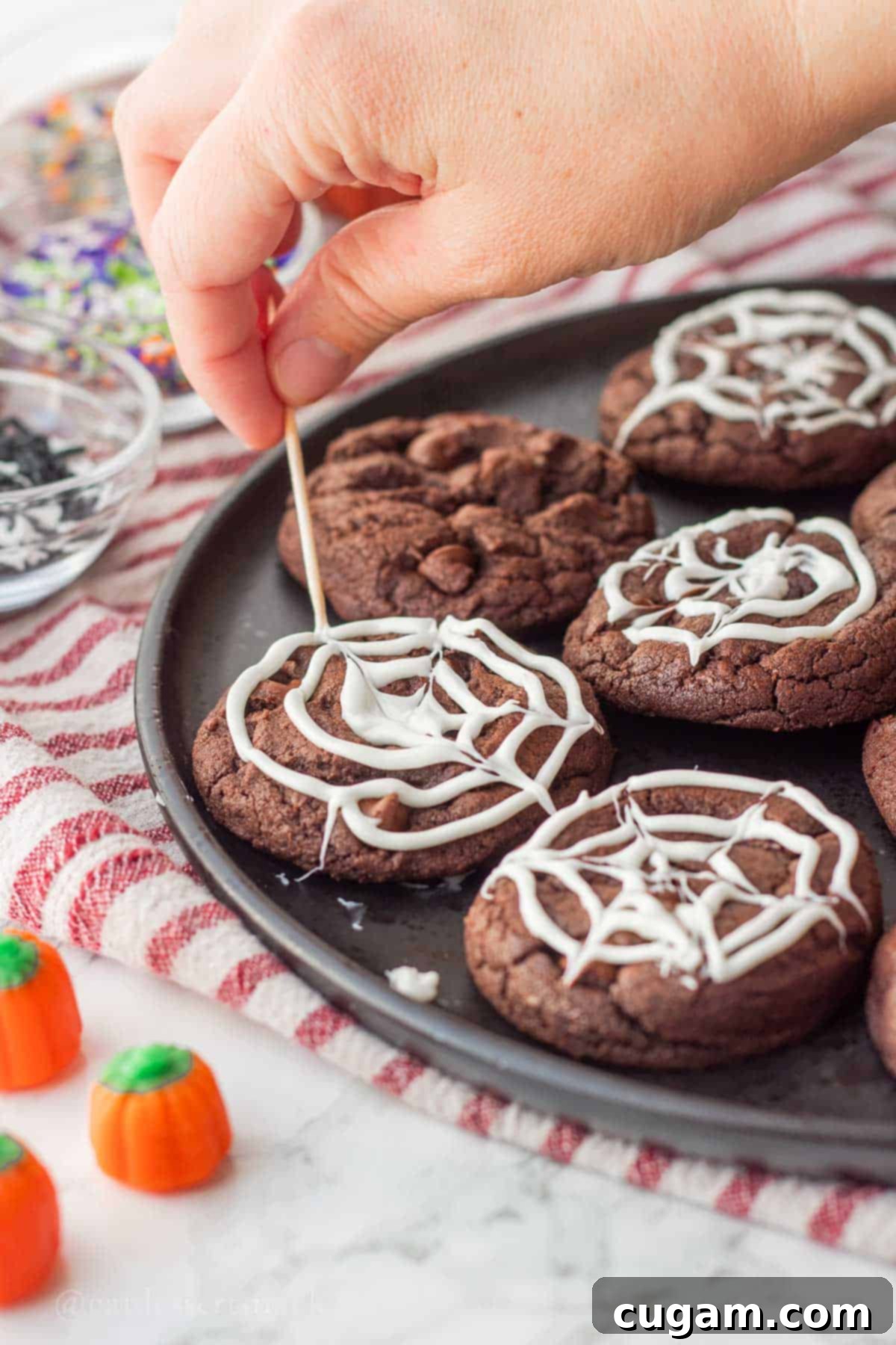 Spooky Spider Web Cookies 11 A toothpick tracing lines from the center outwards through the white chocolate spiral on a baked cookie, forming a distinct spider web design.