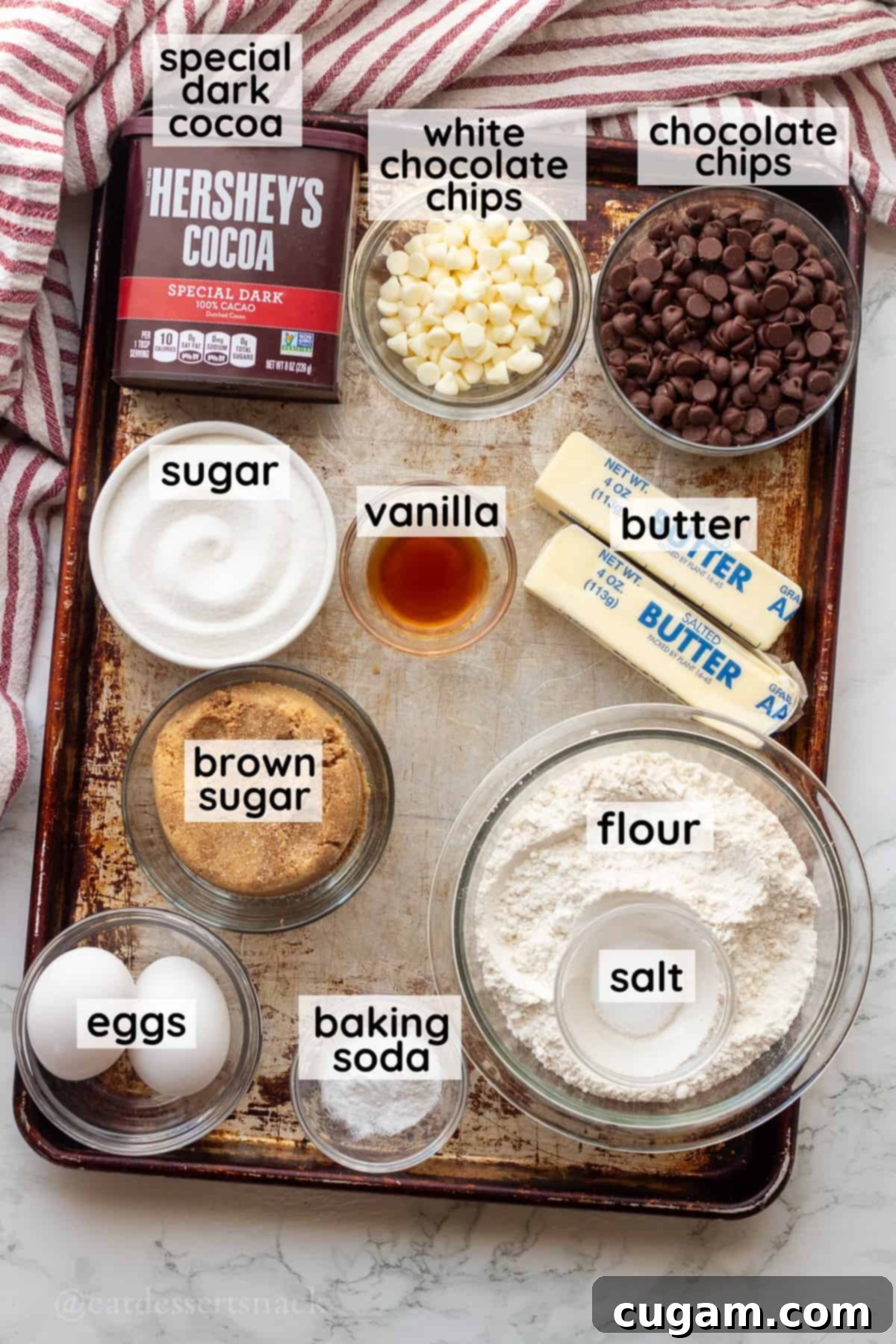 Spooky Spider Web Cookies 3 Labeled ingredients for Halloween spider web cookies arranged in glass bowls on a metal baking tray, including flour, eggs, cocoa powder, white and semi-sweet chocolate chips, butter, and brown and granulated sugars.