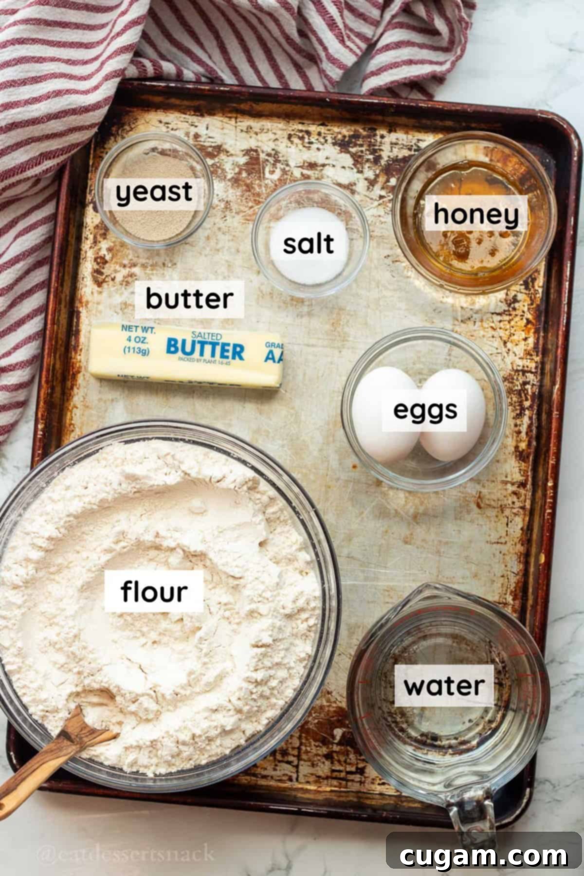 Labeled glass dishes neatly arranged, showcasing all the key ingredients: flour, honey, yeast, water, butter, eggs, and salt, ready for making easy dinner rolls.