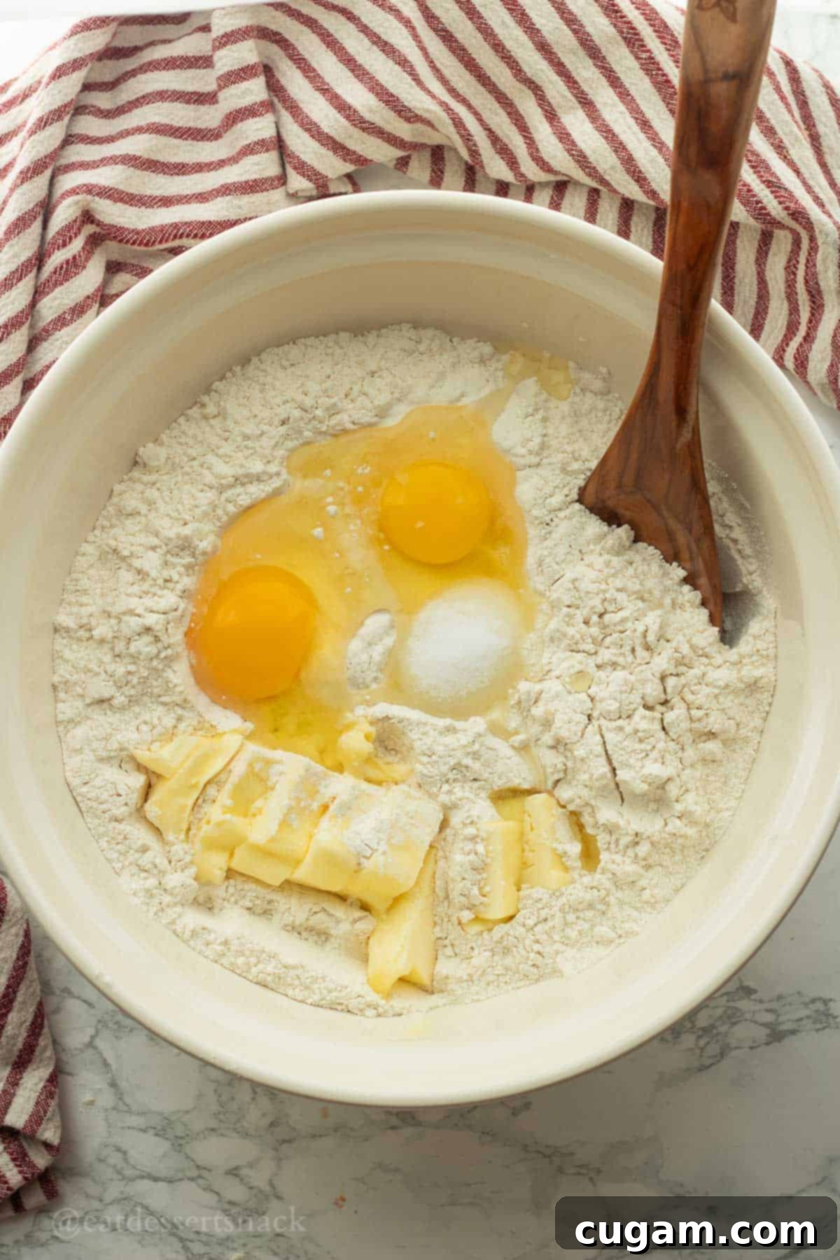 Softened butter, large eggs, all-purpose flour, and salt are carefully placed in a large white mixing bowl, ready to be combined with a wooden spoon.