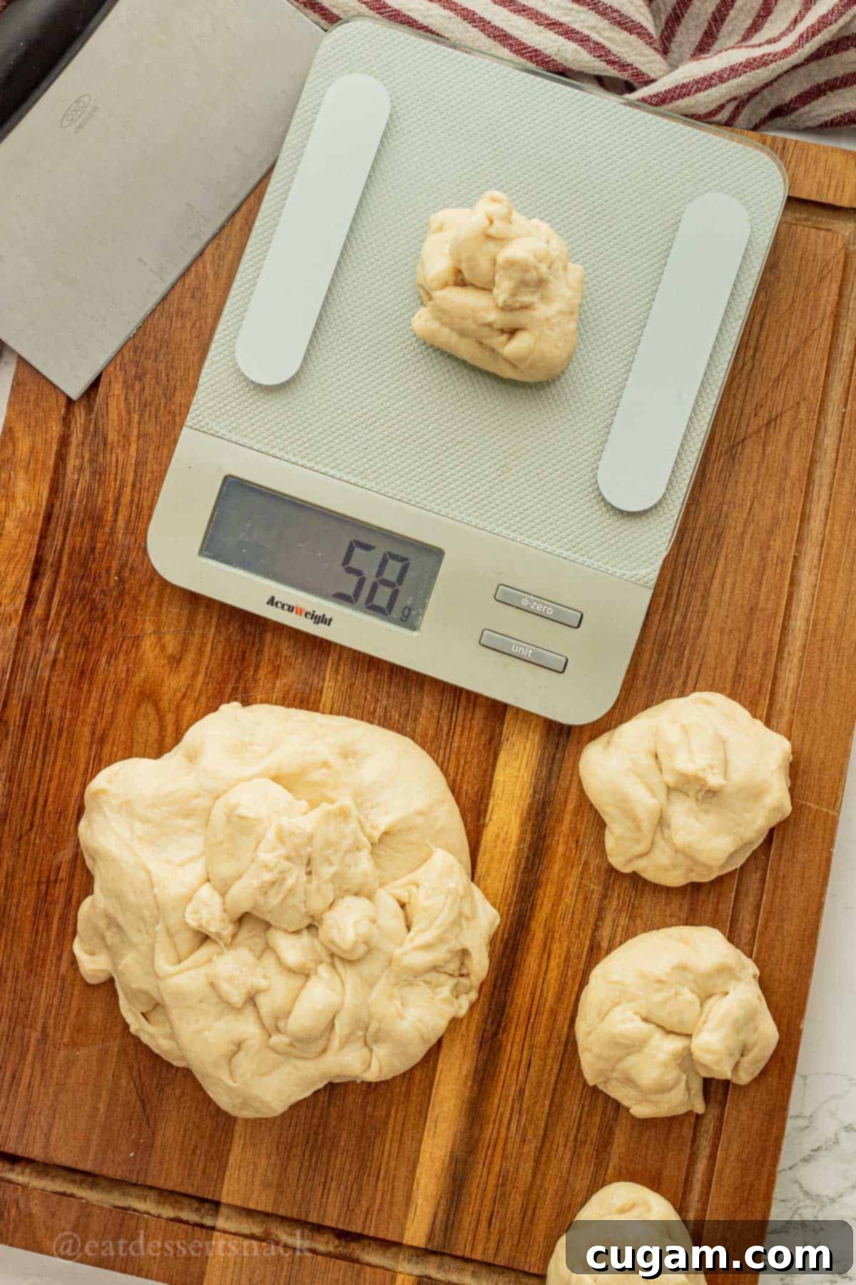 A digital kitchen scale weighing a portion of raw roll dough, with other perfectly sectioned dough balls arranged on a cutting board, ready for shaping.