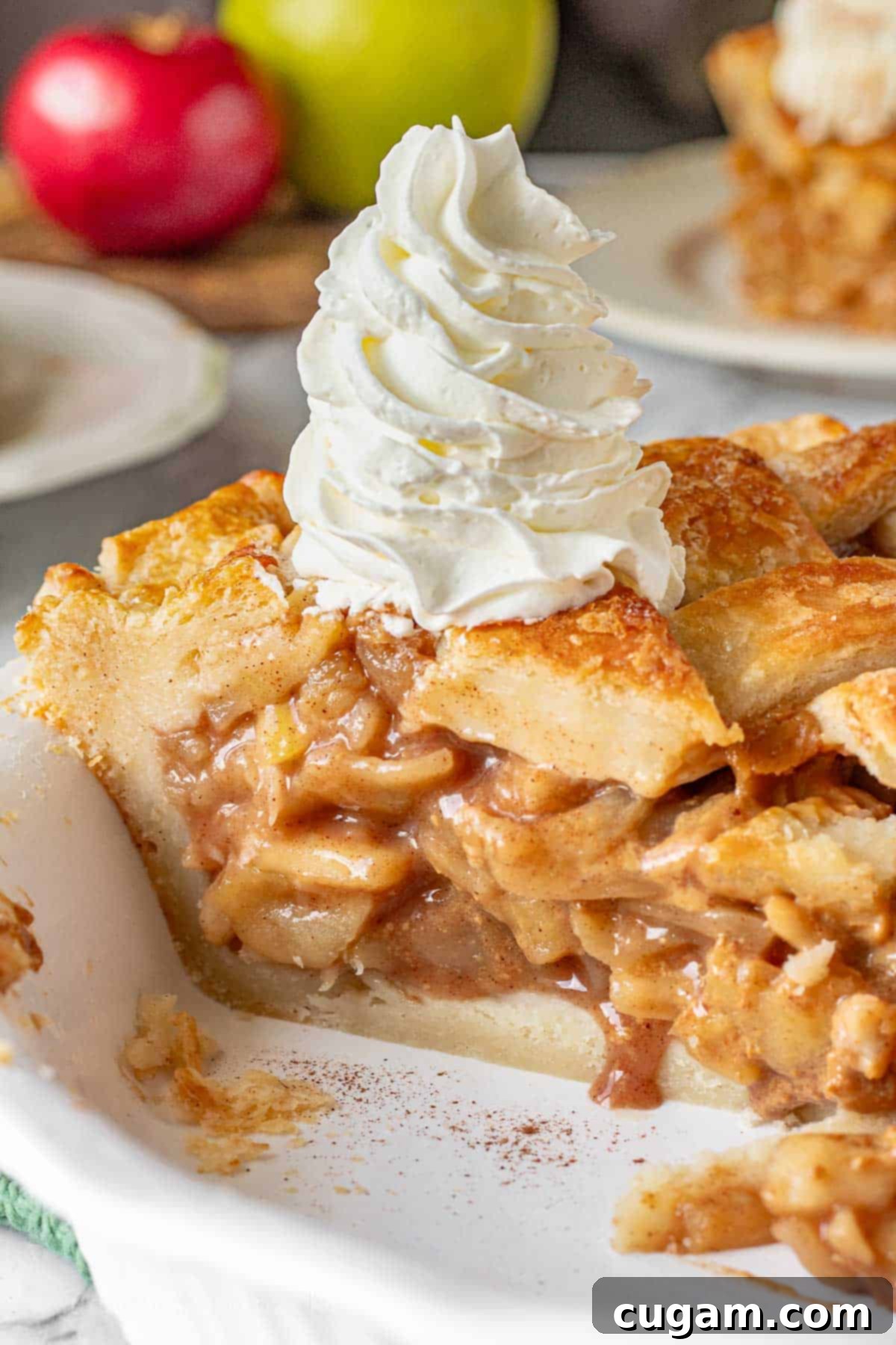 Baked caramel apple pie slice with tall whipped cream, showcasing its rich filling and golden crust.