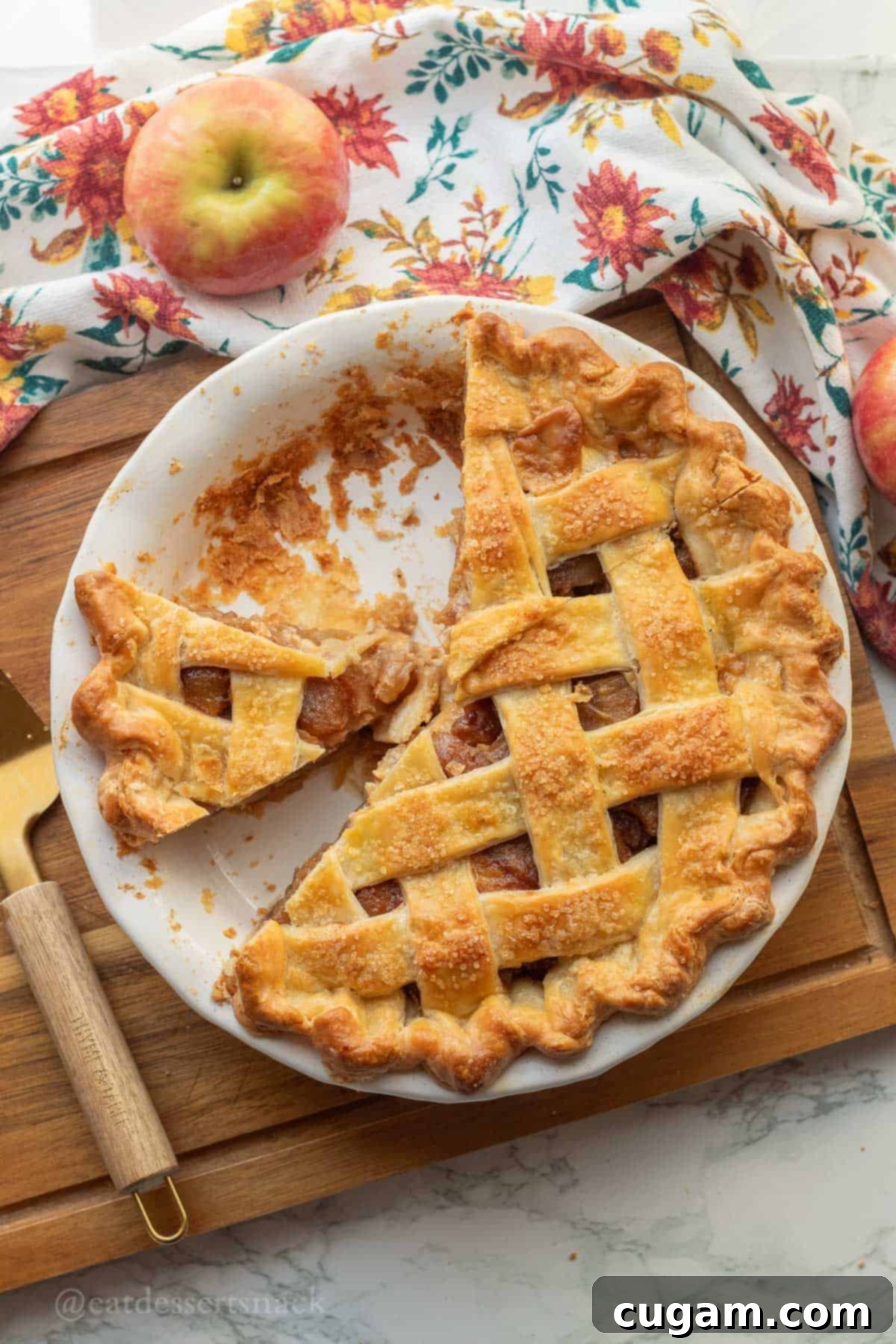 Baked caramel apple pie in white pie dish on wood cutting board, ready to be sliced.