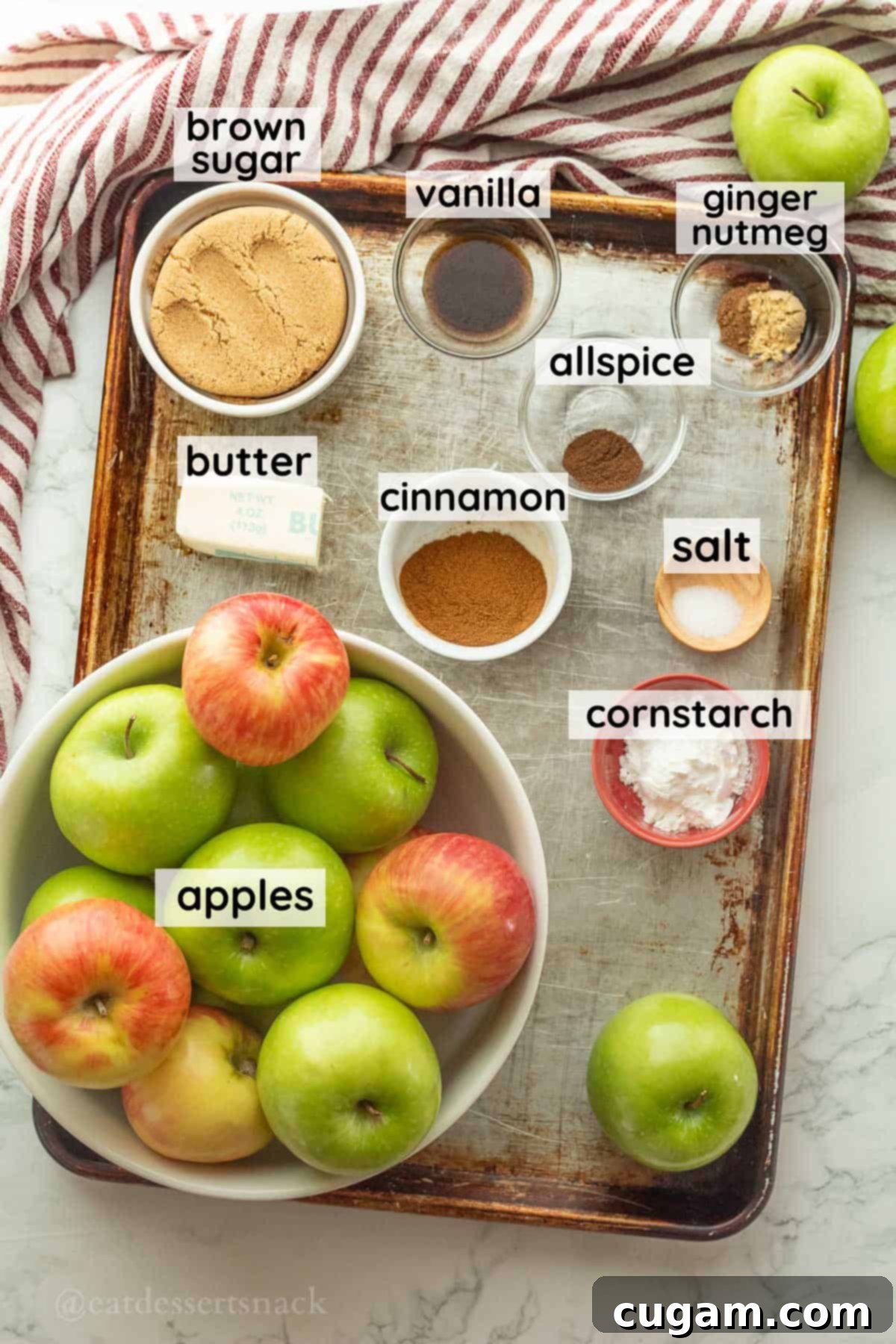 Labeled ingredients for homemade apple pie in glass bowls on metal baking sheet.