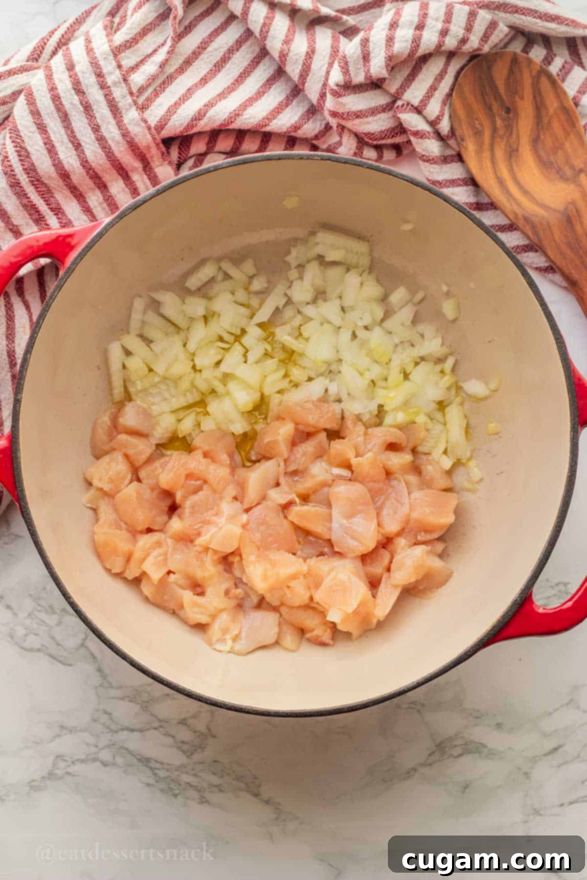 Raw chicken pieces, diced onions, and olive oil being sautéed in a vibrant red Dutch oven.