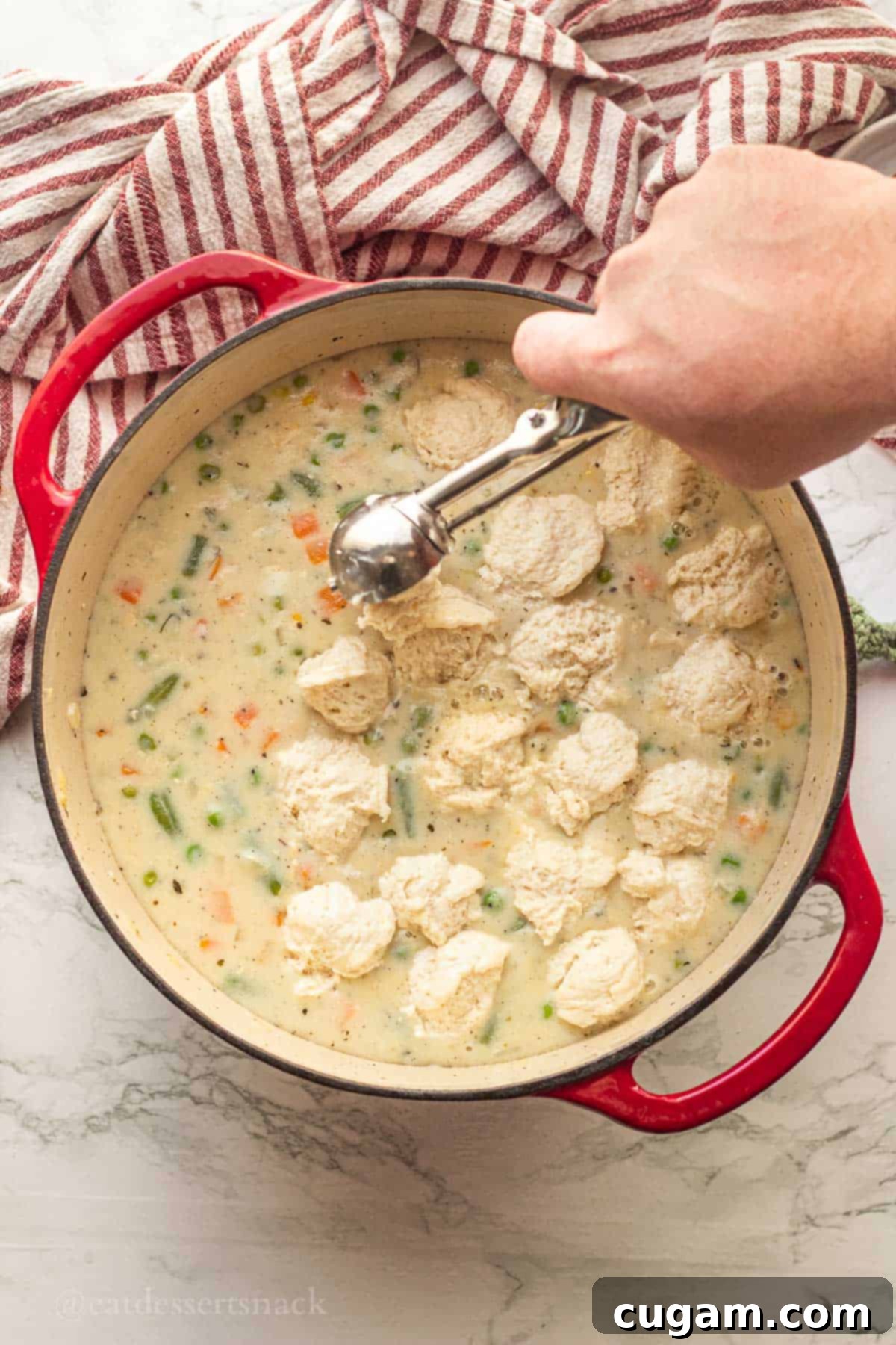 Scooping raw dumpling dough directly into the hot, creamy chicken soup.