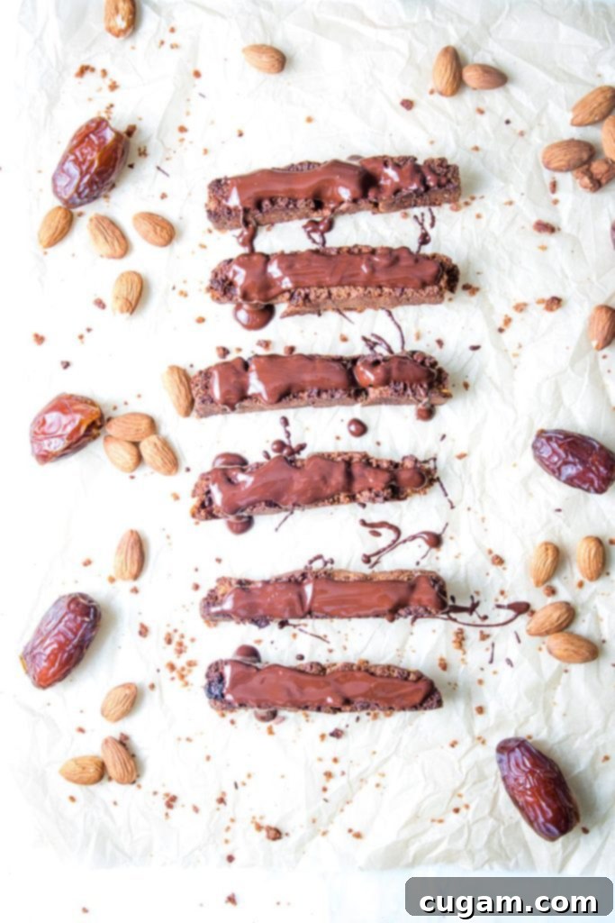 A trio of vegan gluten-free biscotti, some plain and some elegantly drizzled with dark chocolate, alongside raw Medjool dates and almonds, highlighting the natural ingredients.