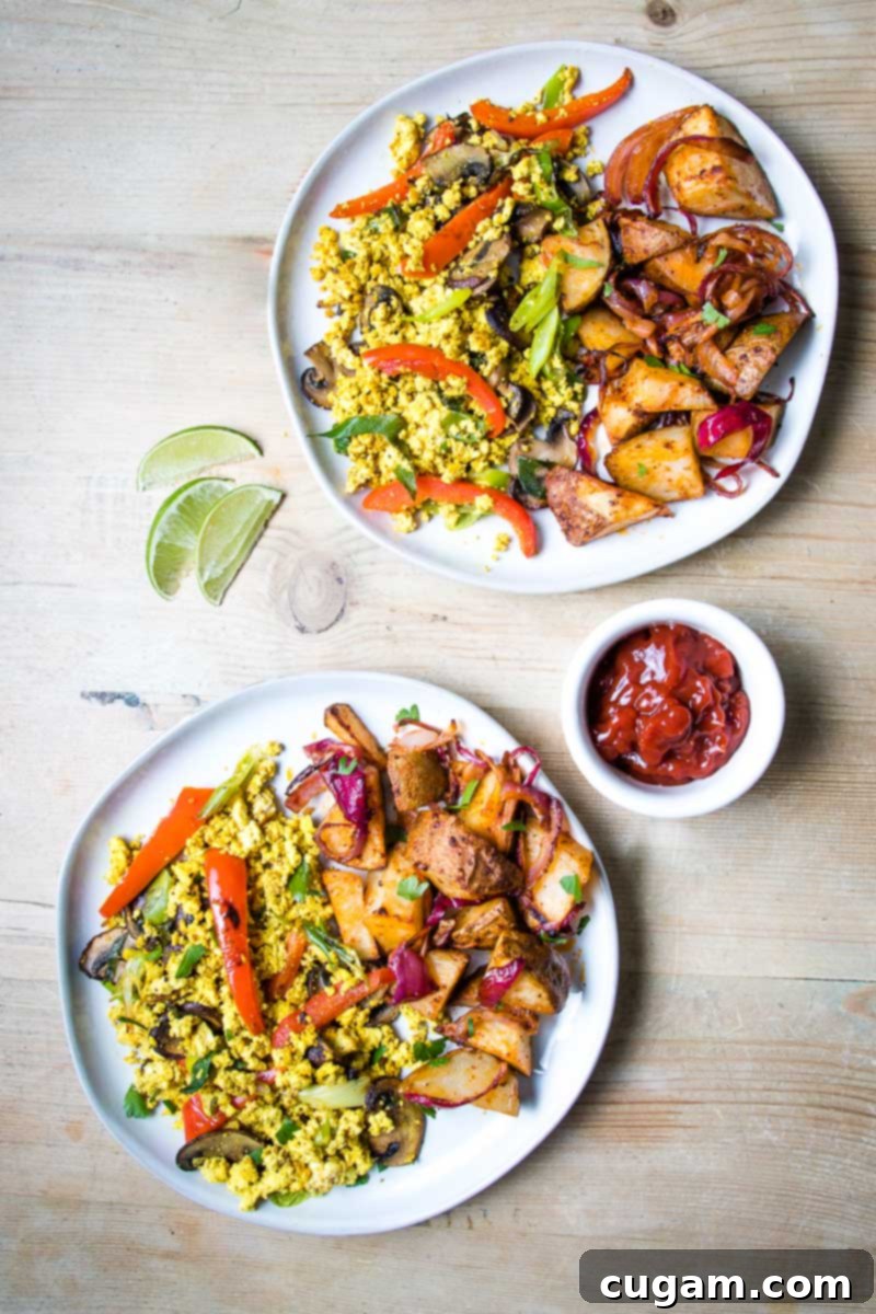 Two white plates on a wood table loaded with colorful veggie scramble and potatoes plus a dish of ketchup