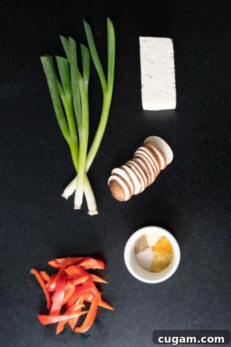 Assorted ingredients for tofu scramble: a block of tofu, fresh mushrooms, red bell pepper, scallions, and various spices.