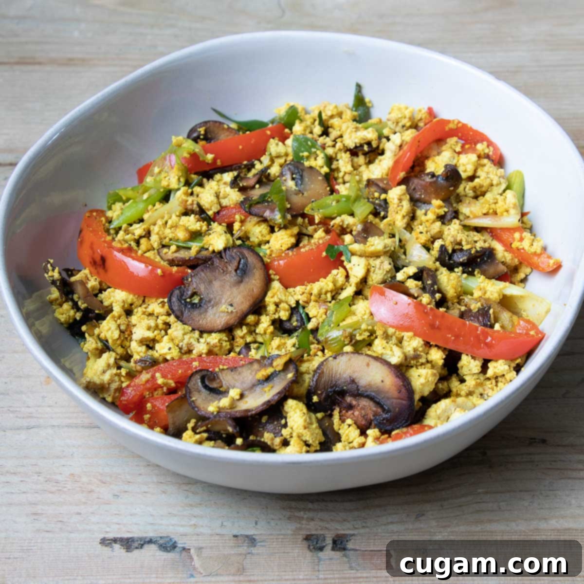 Sauteed mushrooms, peppers, scallions in a large white bowl with scrambled tofu. 
