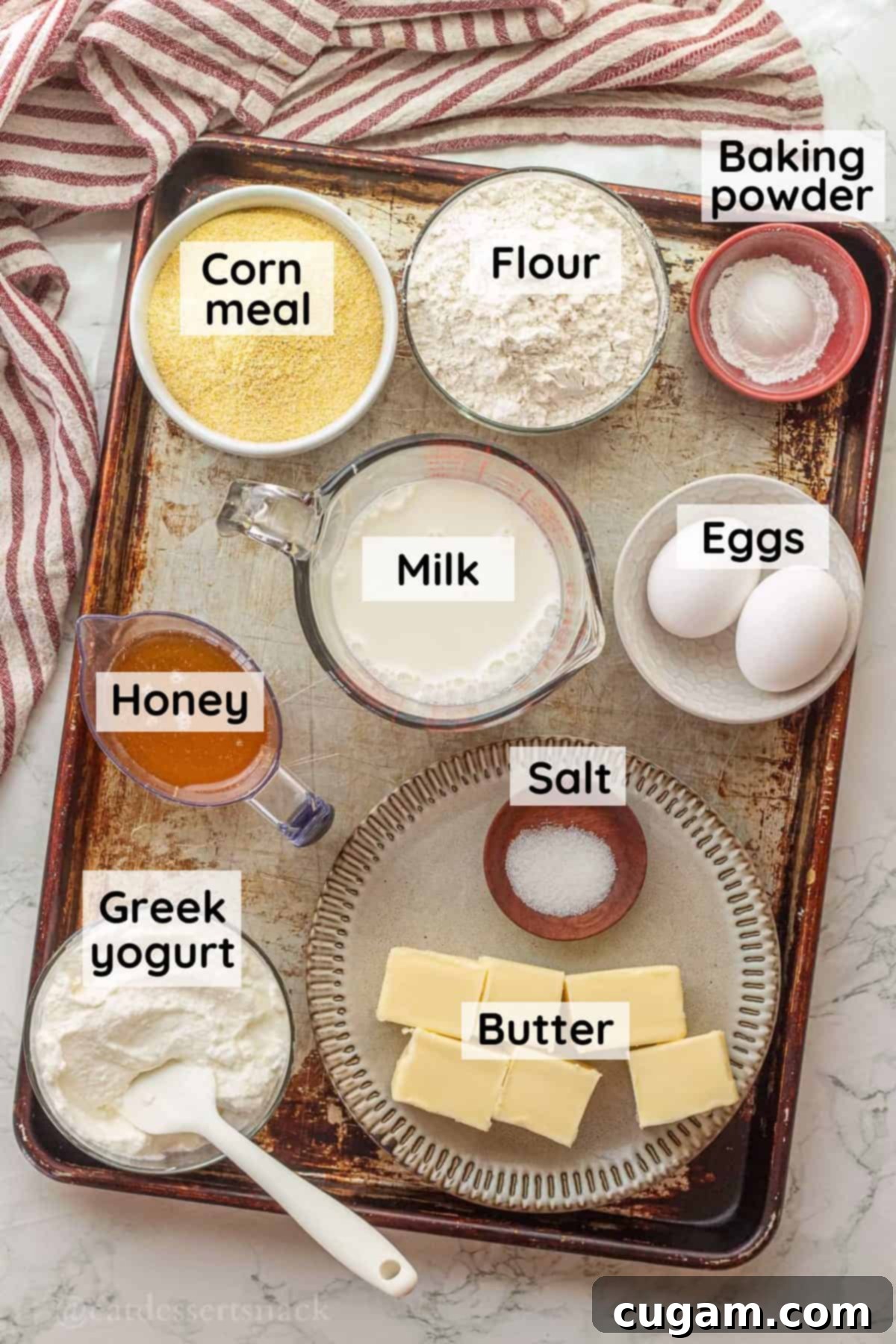 Labeled ingredients for honey butter cornbread in glass bowls on metal baking sheet.