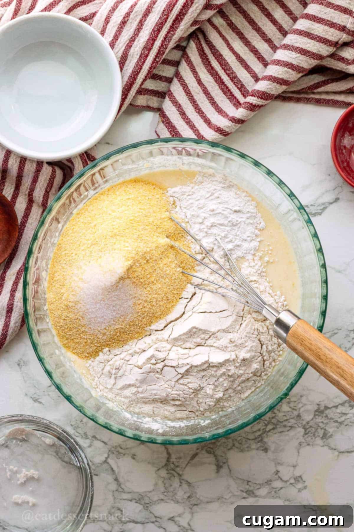 Flour, salt, cornmeal and whisk in glass bowl of liquid ingredients for cornbread.