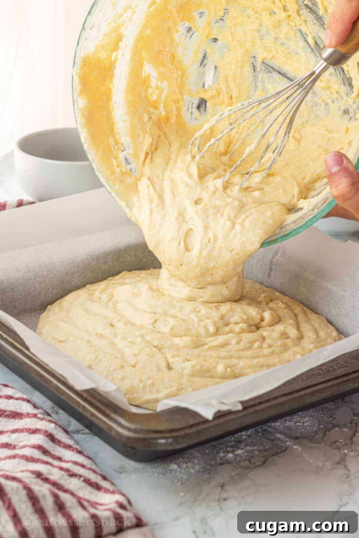 Pouring raw cornbread batter into metal pan.