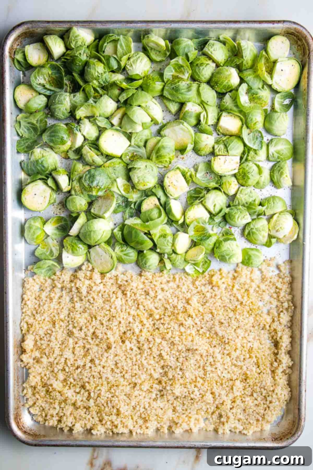 Large baking tray half filled with quinoa, the other half with trimmed brussel sprouts.