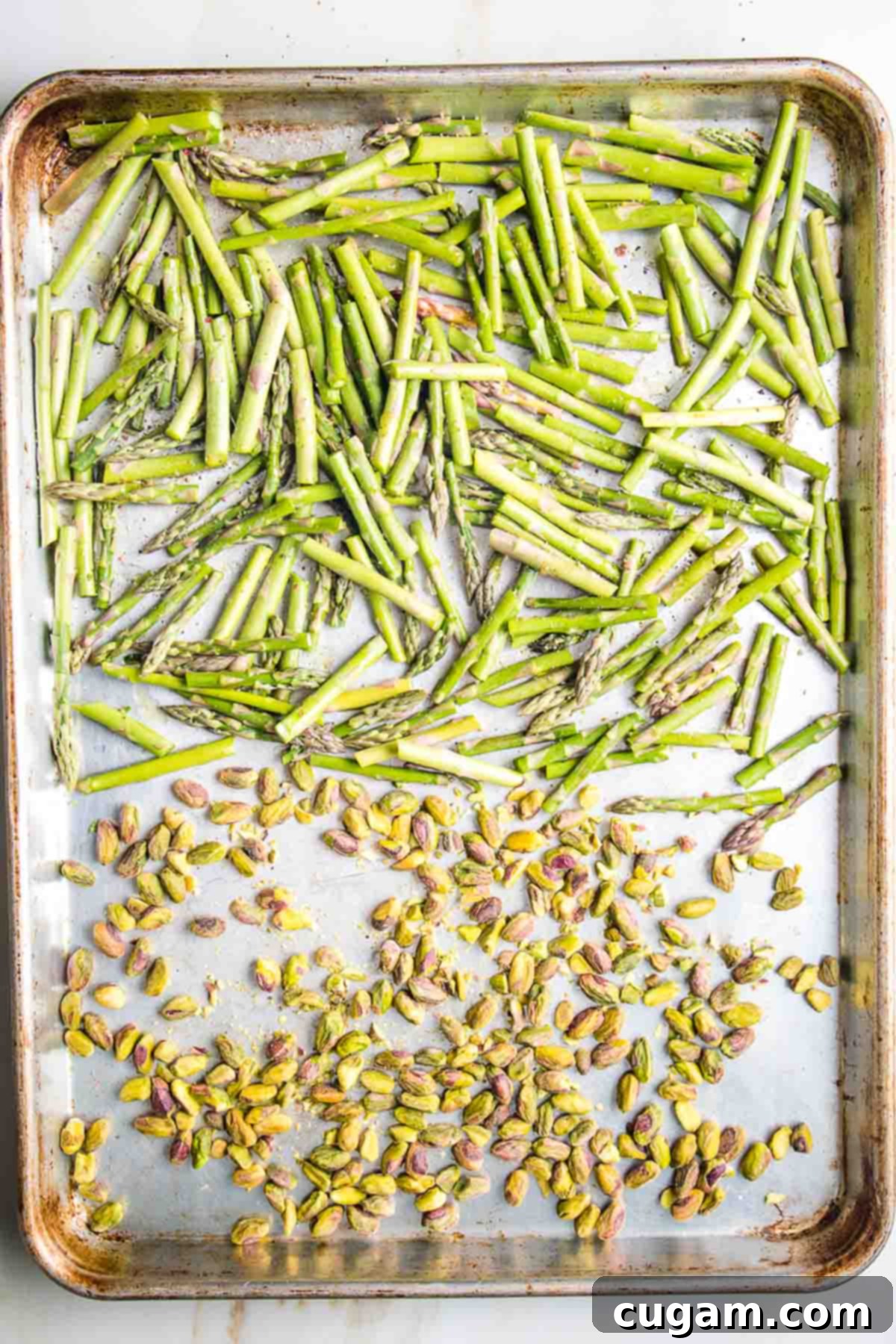 Large baking tray with asparagus pieces and pistachios.