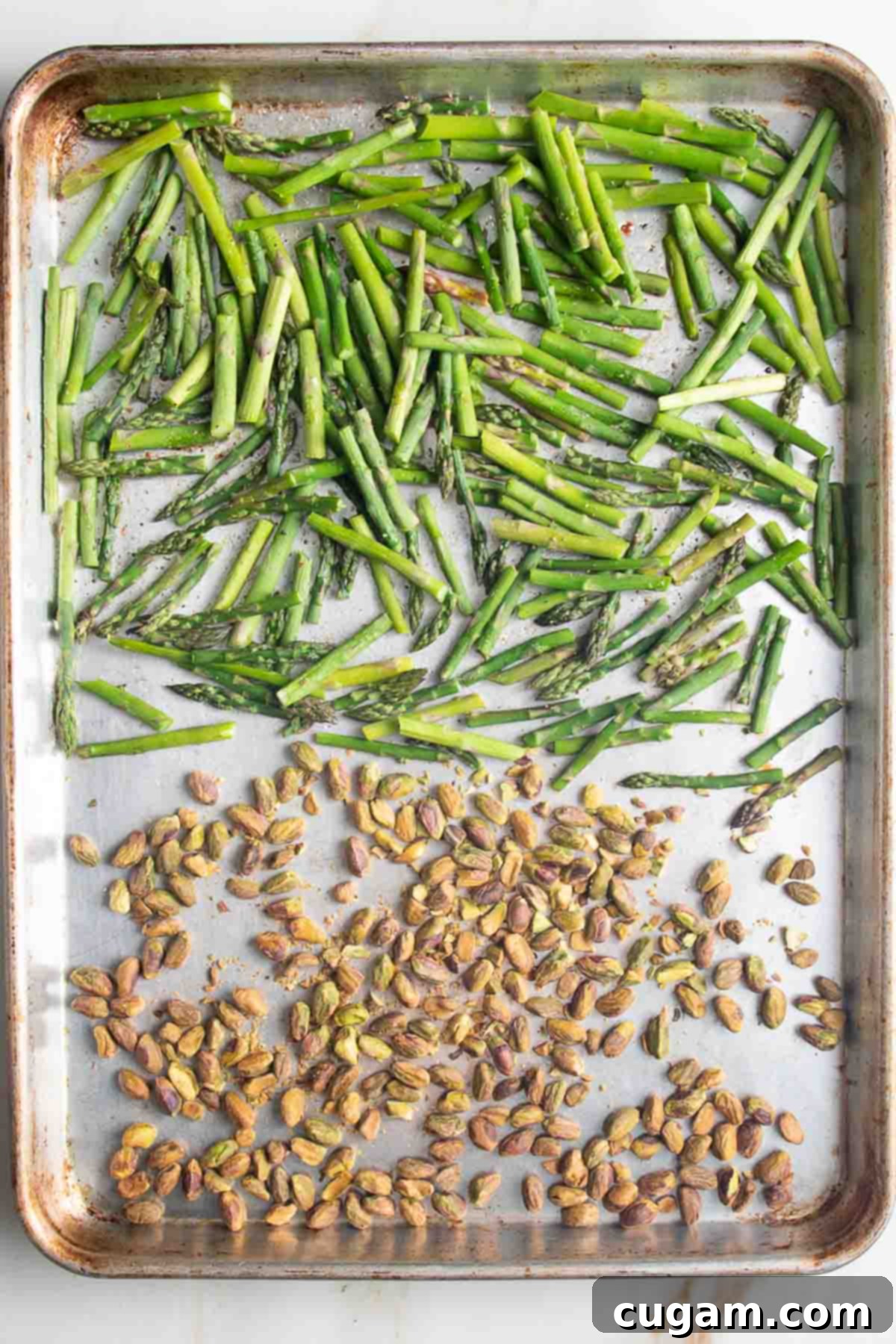 Large baking tray with roasted asparagus pieces and pistachios.