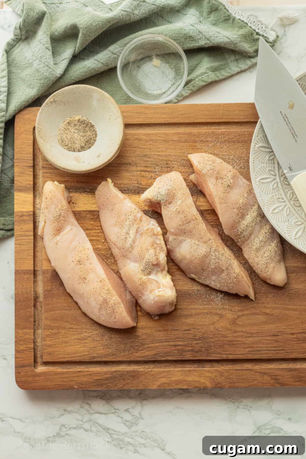 Cut and seasoned raw chicken breasts on wood cutting board.