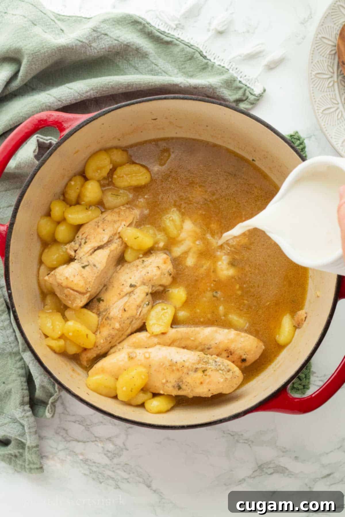 Pouring milk into pot of gnocchi and chicken.
