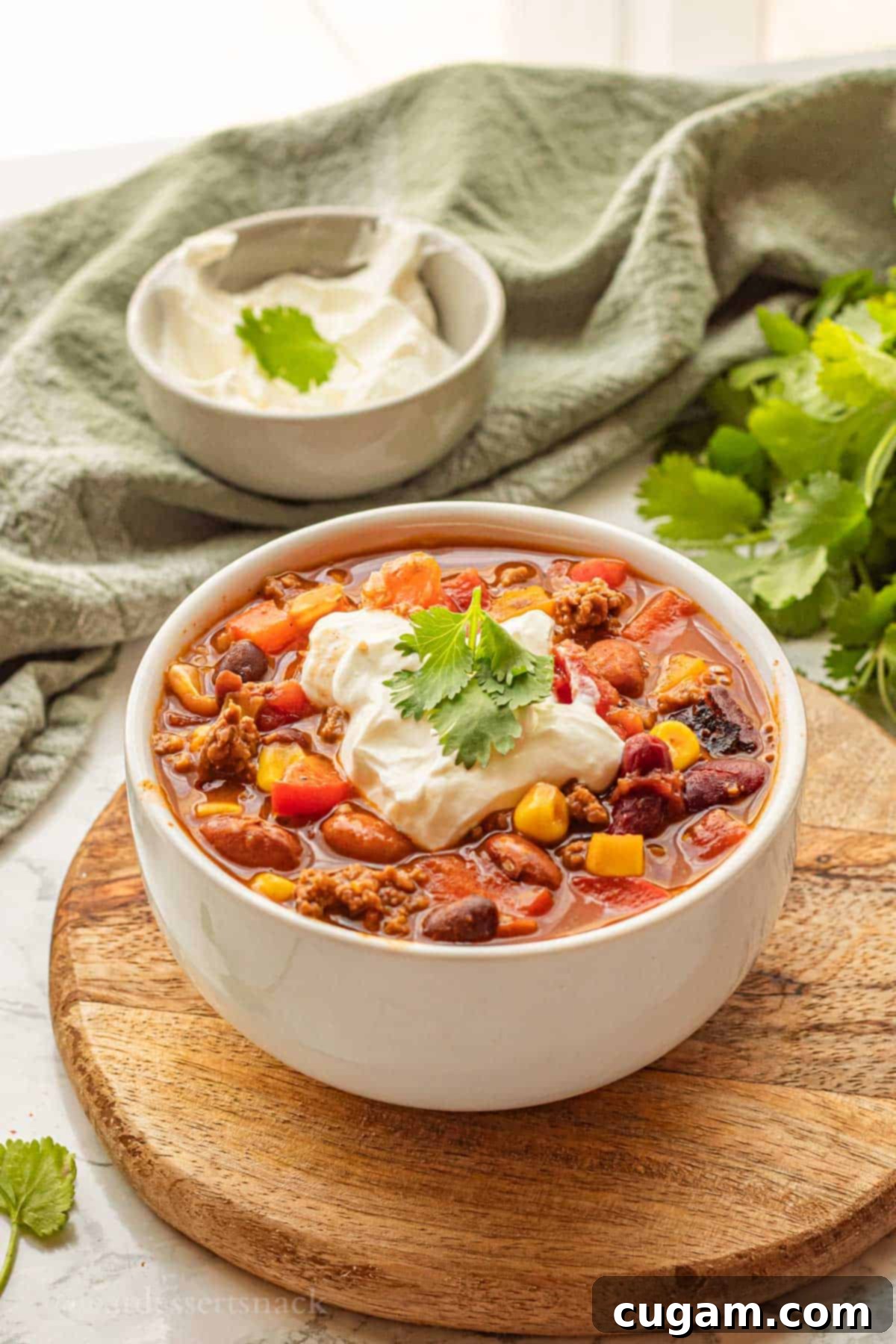 A bowl of healthy taco soup, garnished with a dollop of sour cream and fresh cilantro, resting on a rustic wooden cutting board.