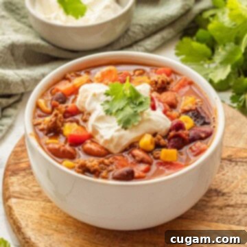 A close-up shot of cooked healthy taco soup served in a white bowl, adorned with a swirl of sour cream and a sprinkle of fresh cilantro on top.