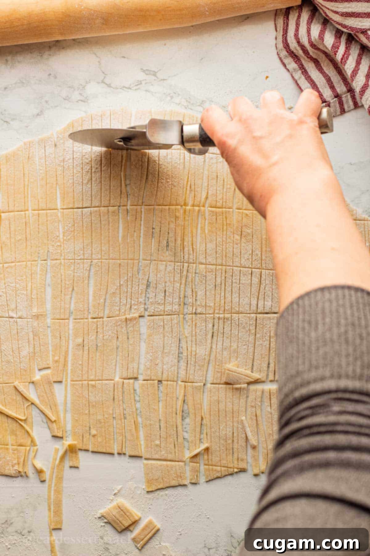 Nourishing Bone Broth Chicken Noodle Soup 10 Cutting egg noodles with pizza cutter on marble surface.