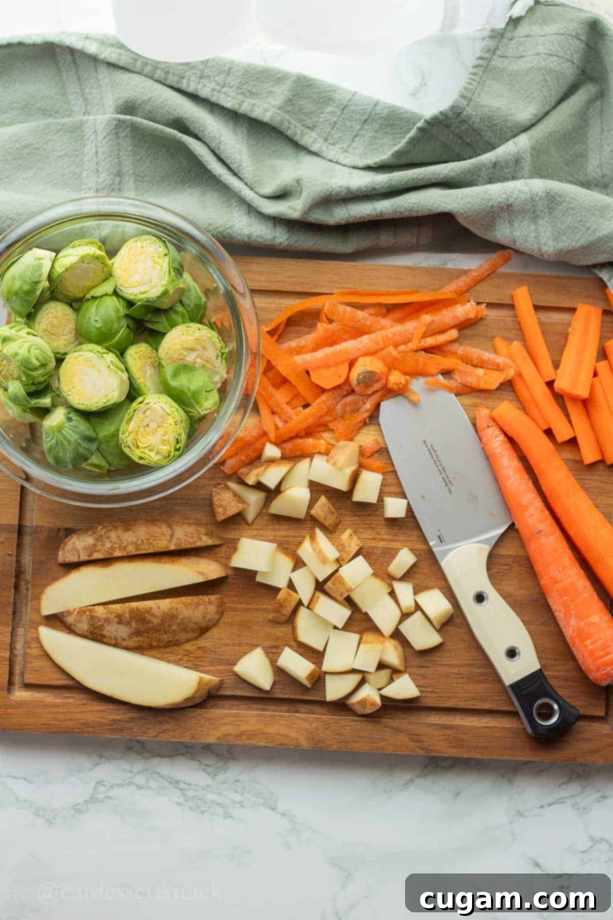 Raw potatoes and carrots meticulously diced on a cutting board, alongside Brussels sprouts, a knife, and vegetable peelings.