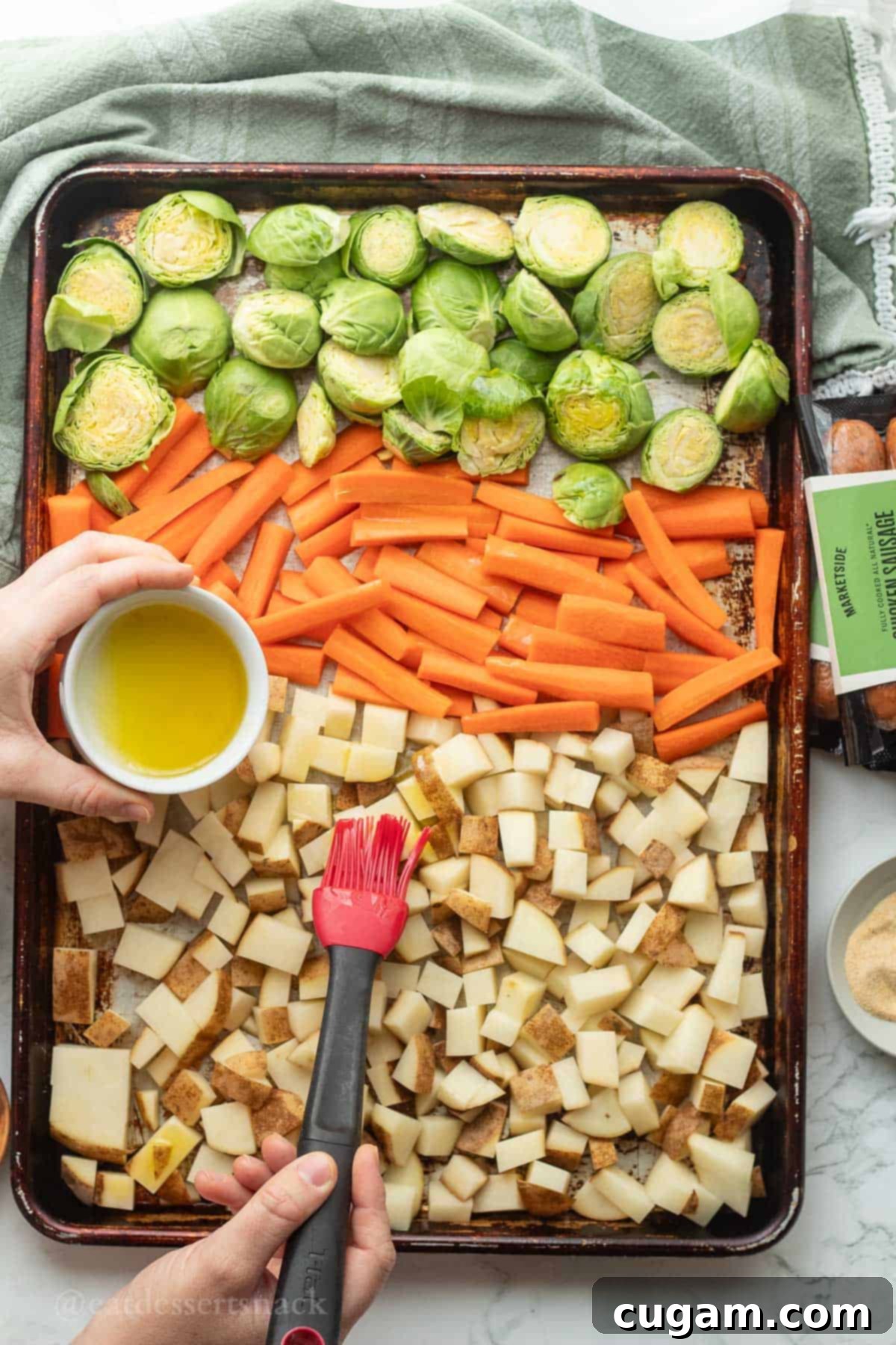 A generous drizzle of olive oil coats raw potatoes, carrots, and Brussels sprouts spread across a metal baking pan.