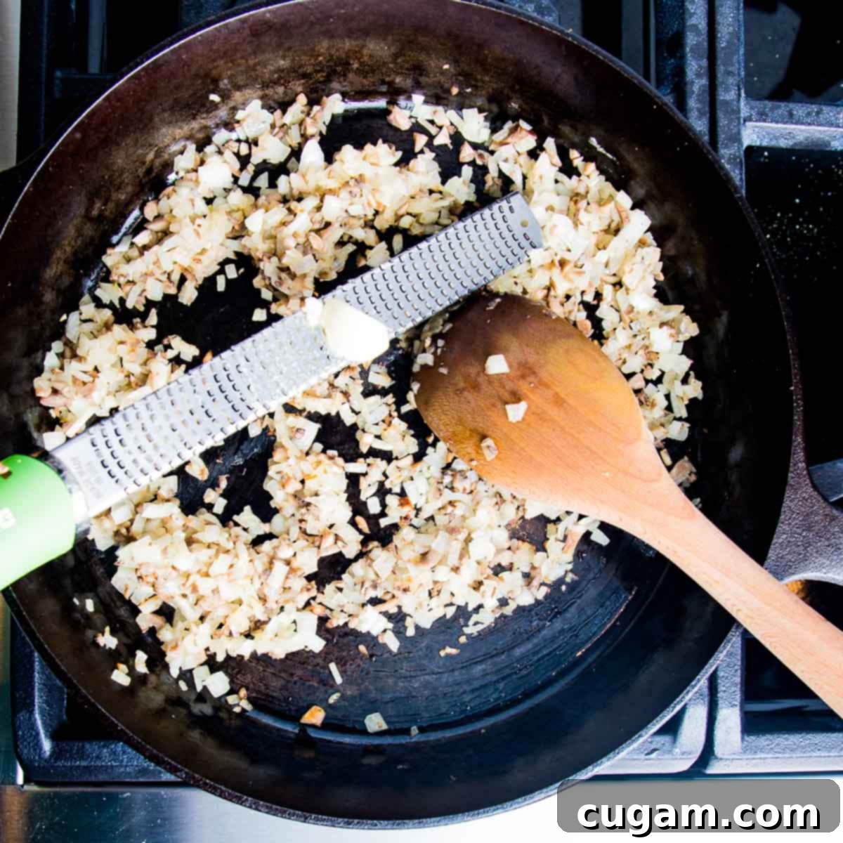Microplane grating garlic over a cast iron skillet with sauteed onions.