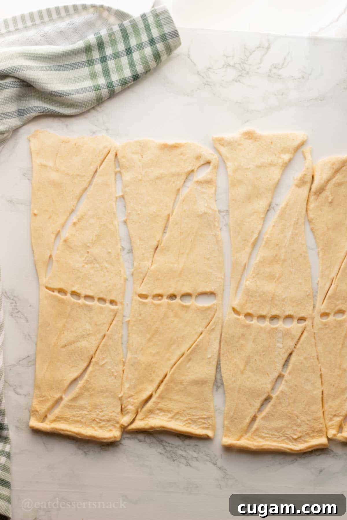 Raw crescent rolls flat on marble countertop.