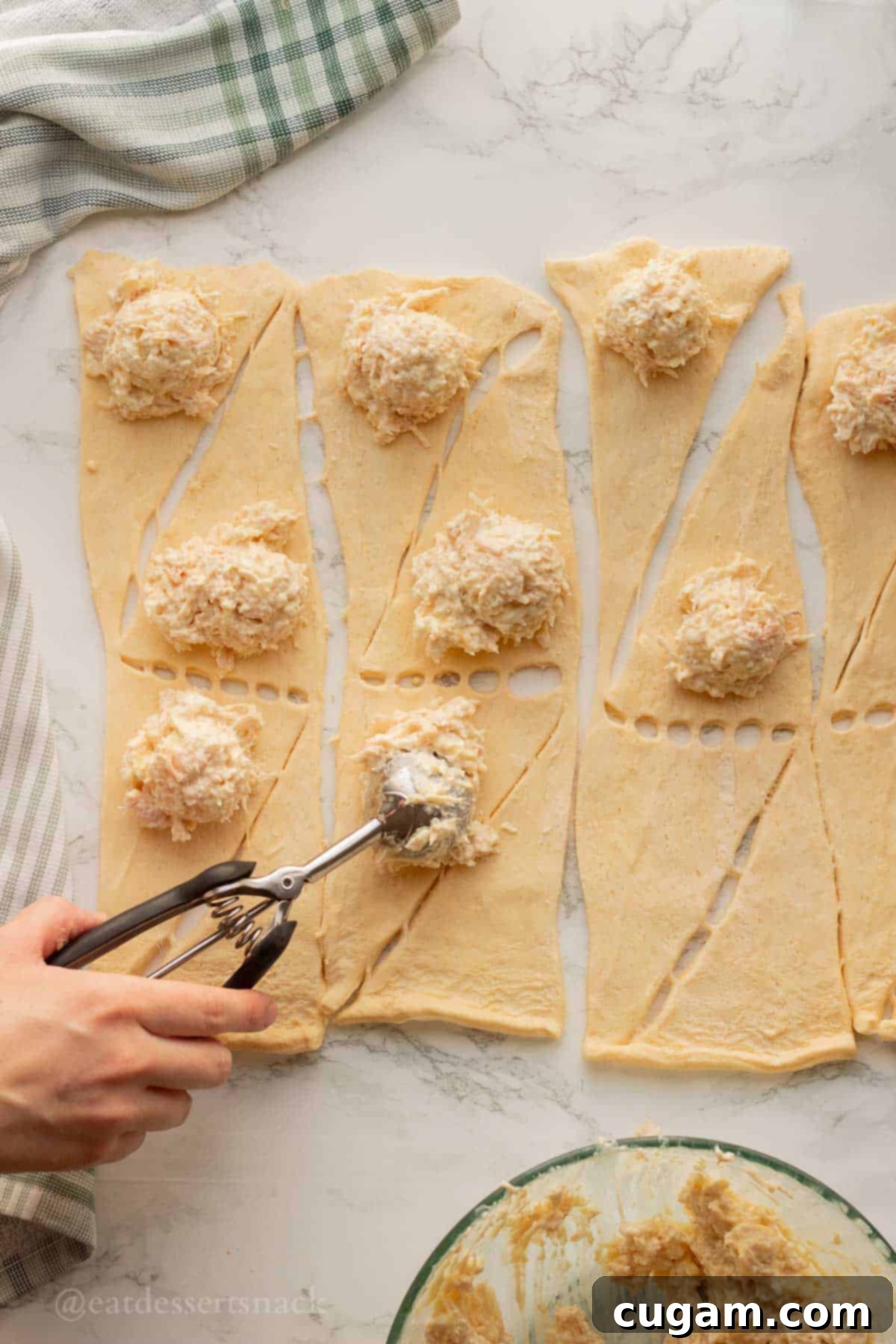 Scooping chicken filling onto raw crescent rolls.