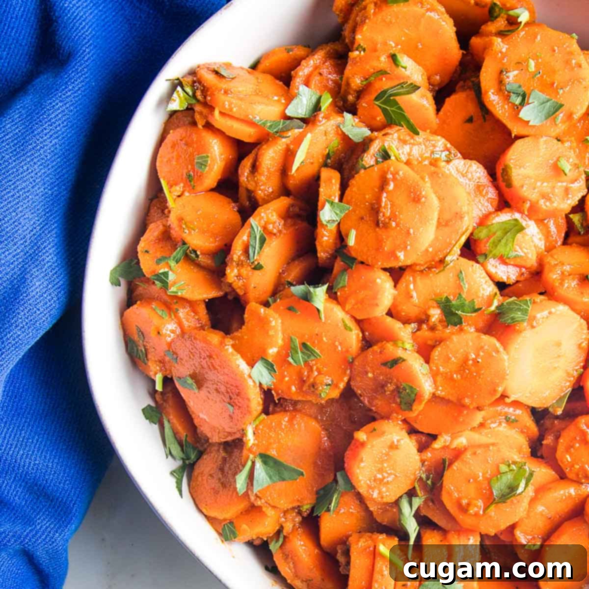 Close up of moroccan spiced carrots in a white bowl, garnished with fresh parsley.
