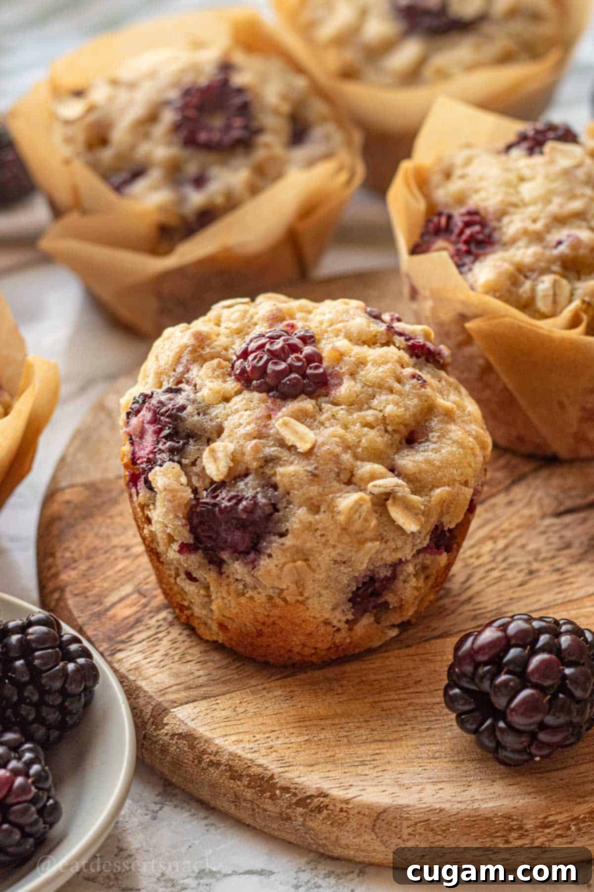 Baked banana blackberry oatmeal muffin on wood cutting board with blackberries.