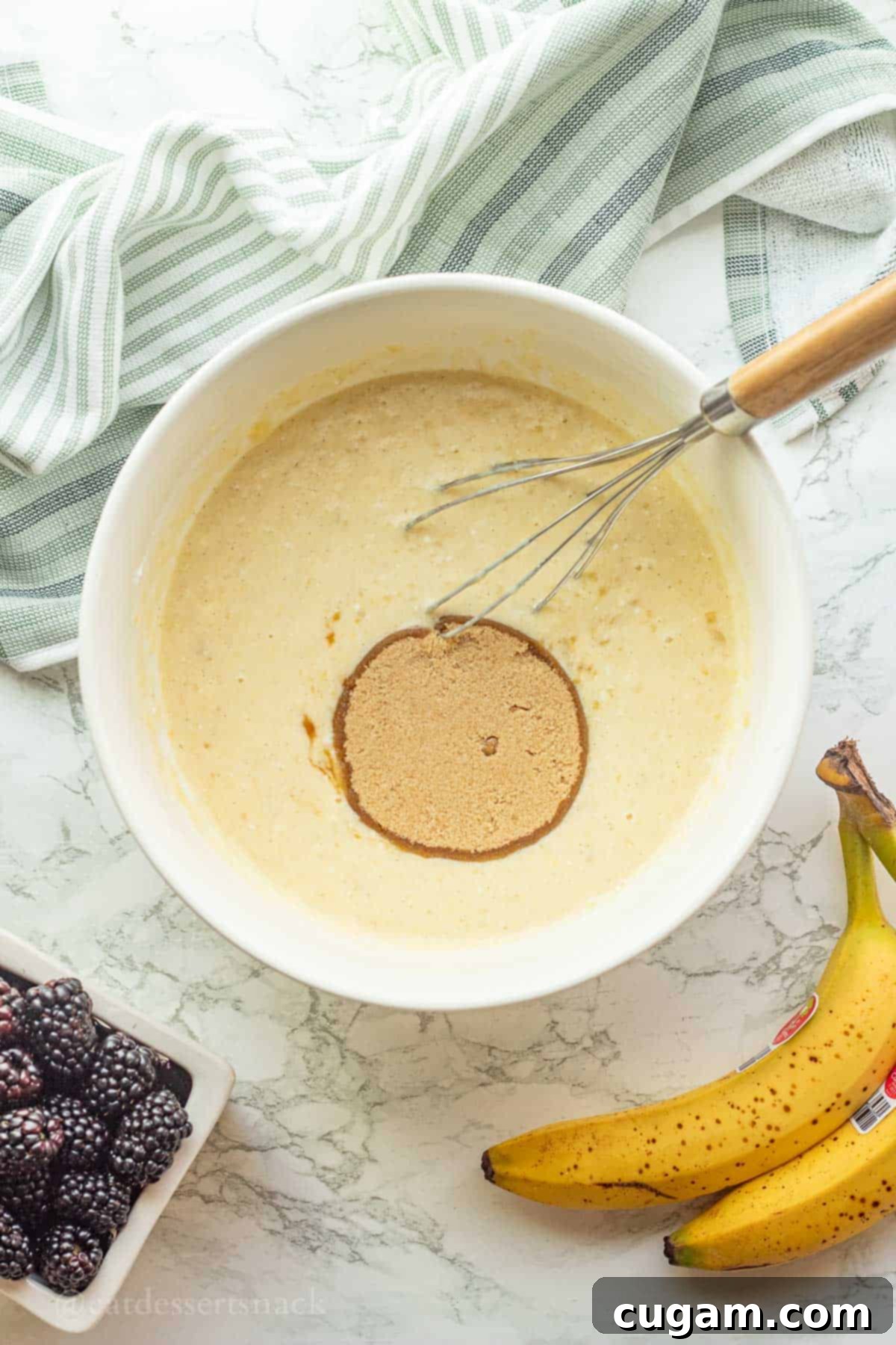 Brown sugar in raw muffin batter in white bowl with whisk.