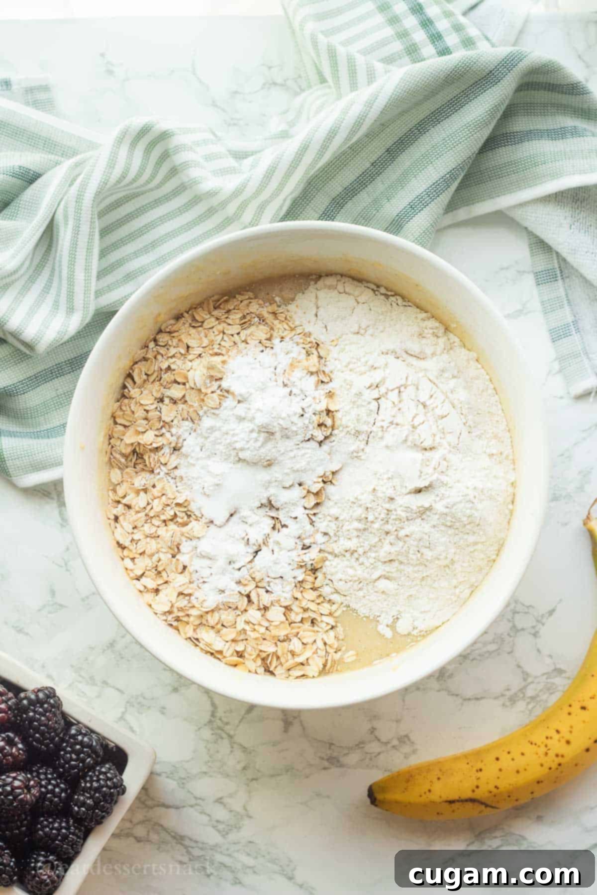 Flour, oats, and baking powder in white bowl of wet muffin batter.