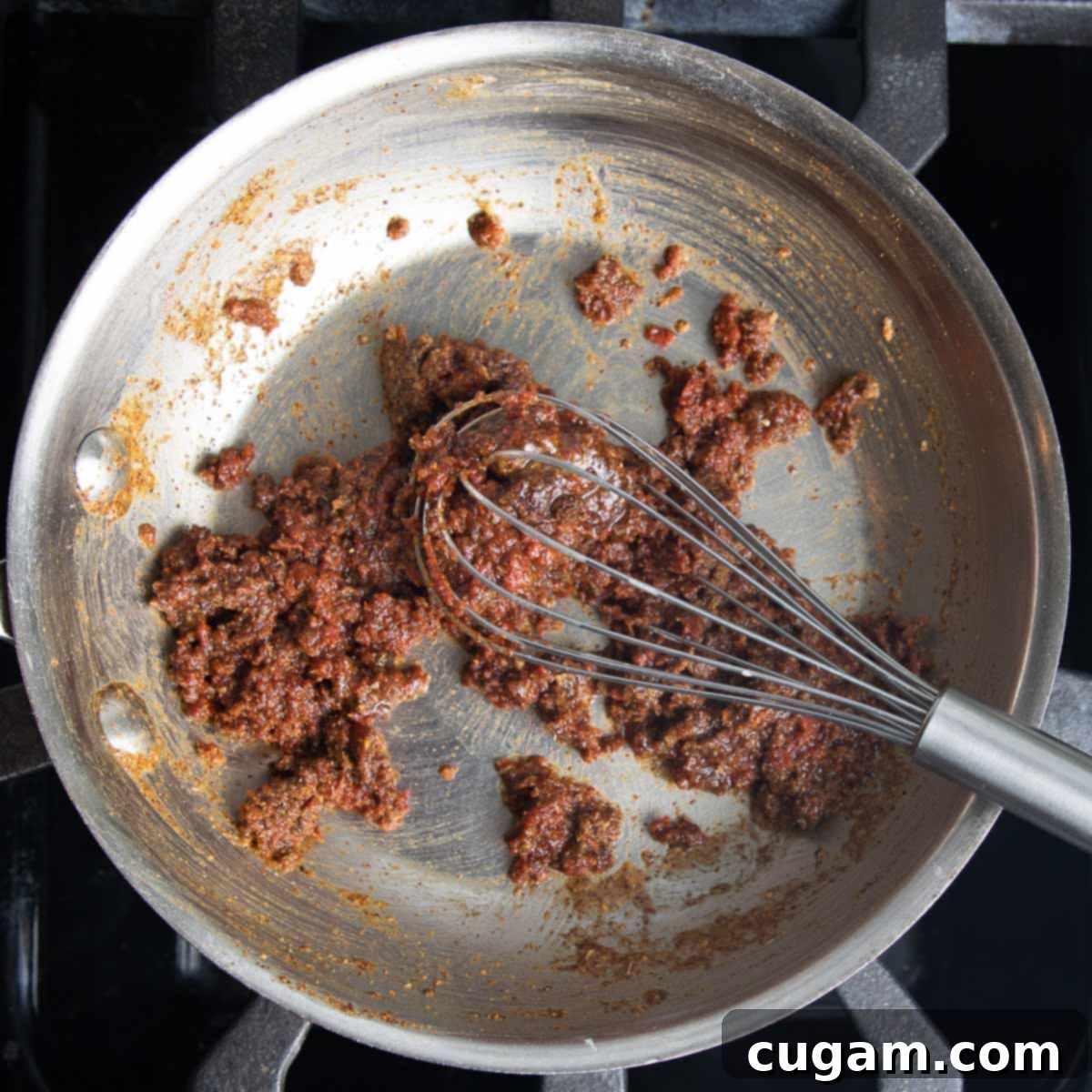 Making enchilada sauce by whisking together tomato paste, spices and roux to form a paste. 