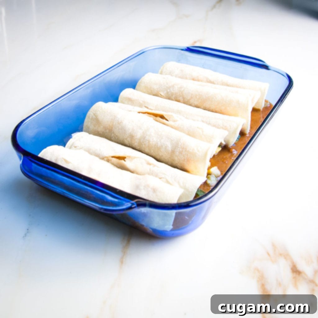 Blue glass casserole dish loaded with enchiladas on top of red sauce. 
