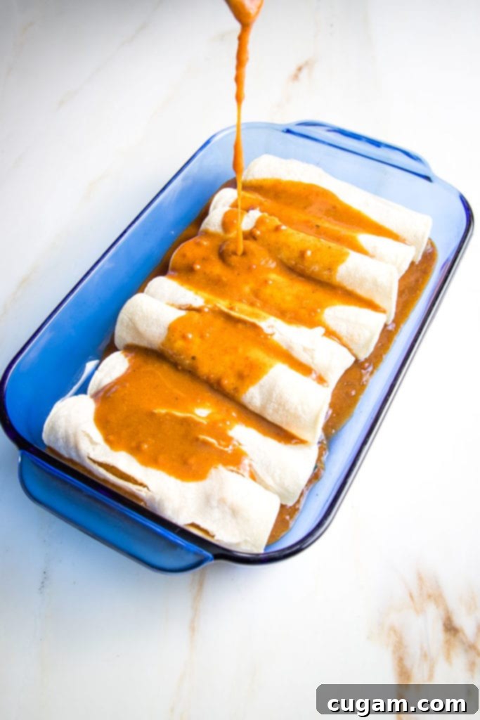 Red enchilada sauce poured on top of veggie filled enchiladas