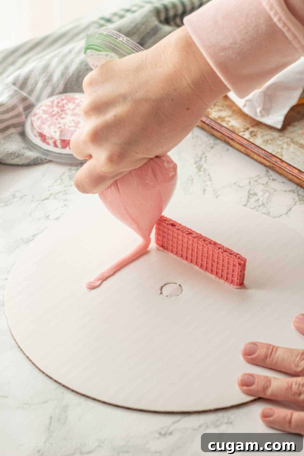 Piping pink frosting onto white plate.