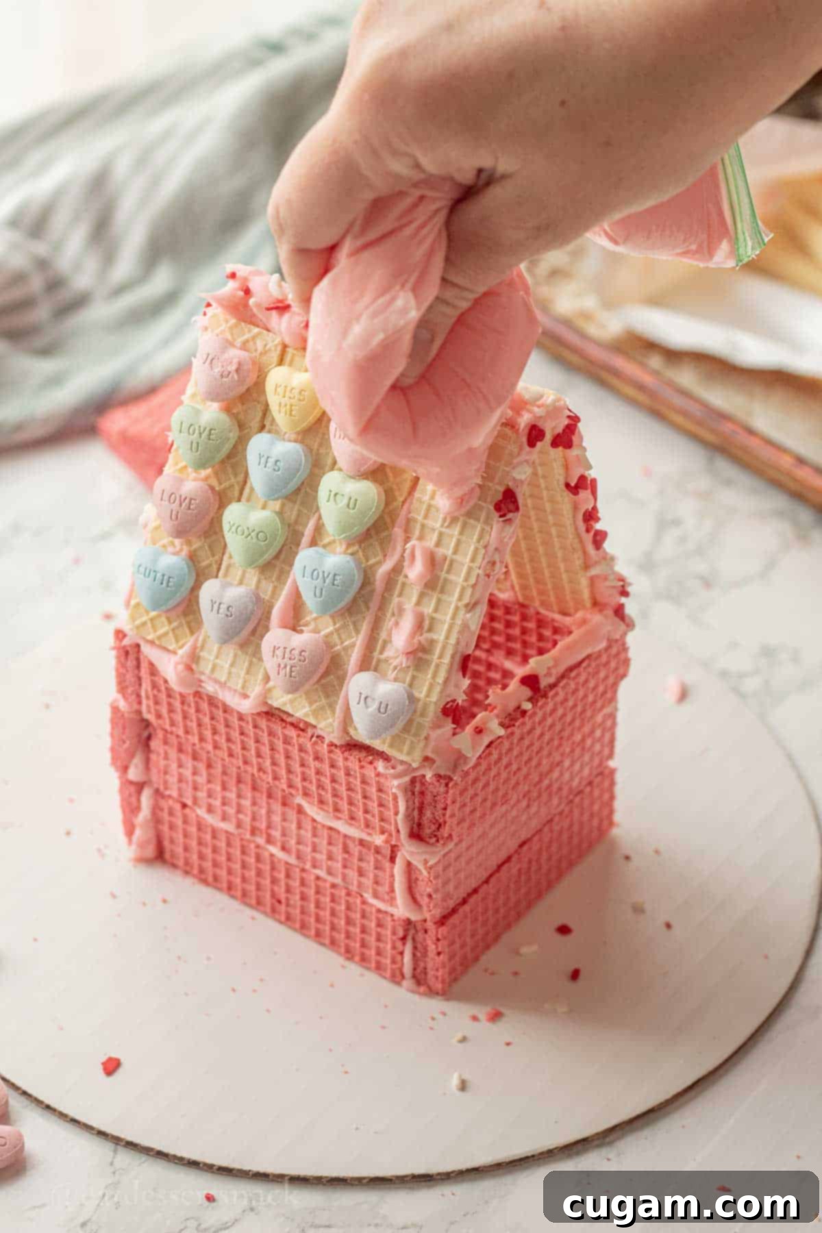 Piping pink frosting onto wafer cookie house roof.