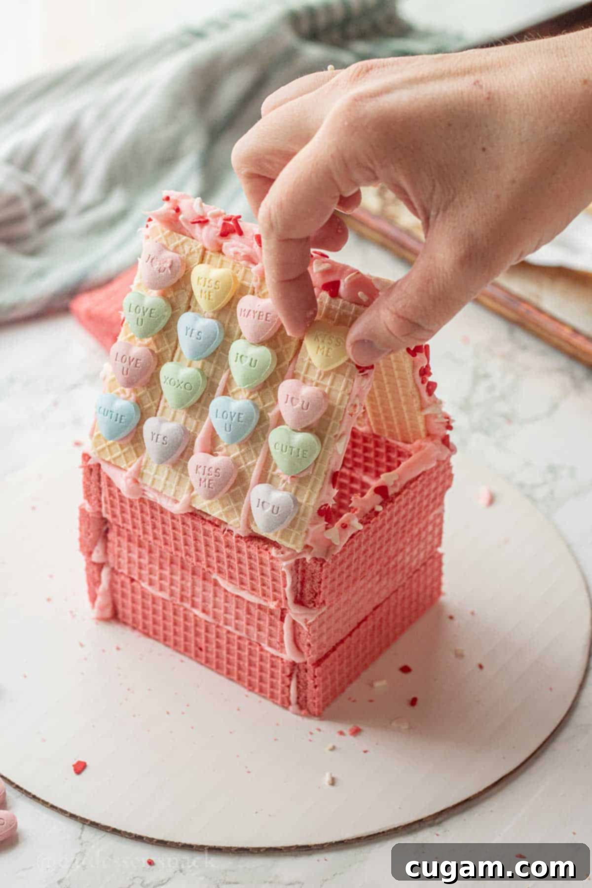 Hand placing hearts onto cookie house roof.