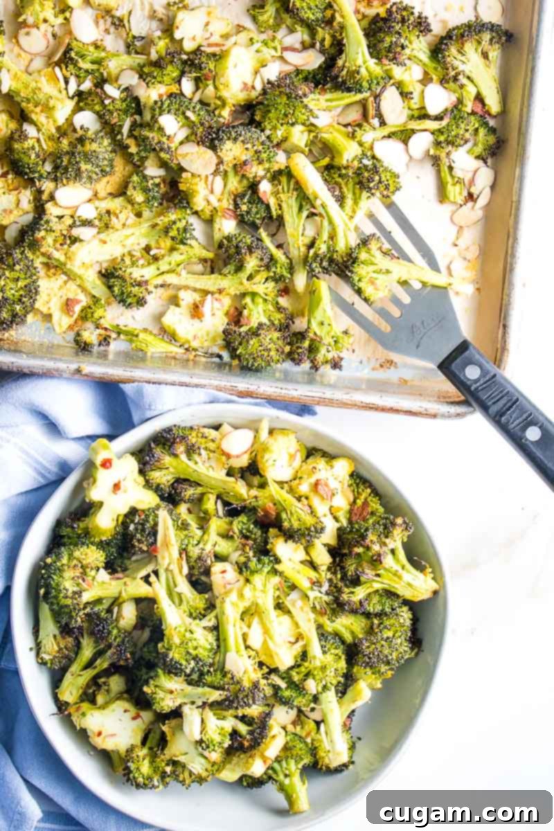 A sheet pan full of perfectly roasted broccoli, golden brown and crispy, with a spatula scooping a portion into a serving bowl, highlighting its readiness to be enjoyed.