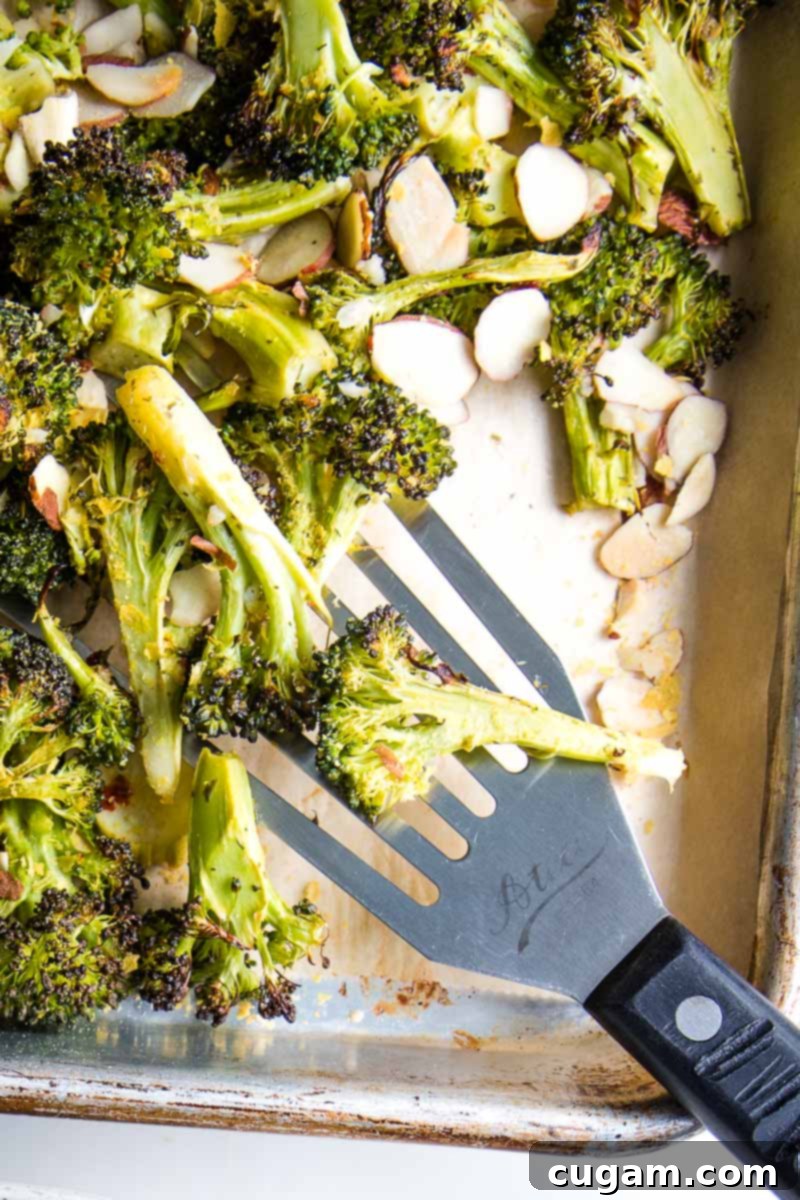 A close-up of beautifully roasted broccoli on a baking sheet, featuring golden brown, crispy edges and a perfect tender-crisp texture, ready to be garnished.