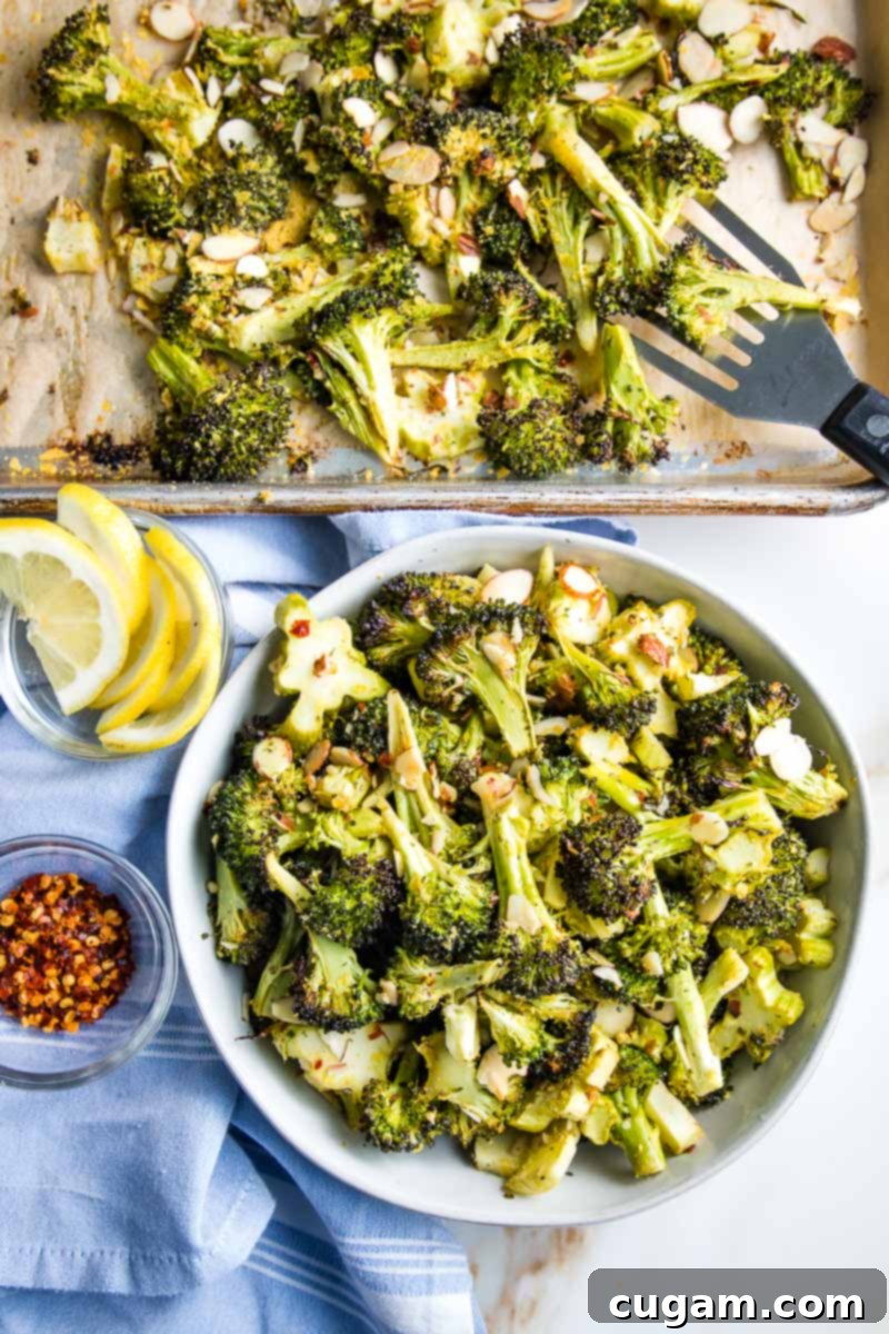 A spatula gently transferring a portion of crispy oven roasted broccoli from the sheet pan into a white serving bowl, showcasing its delicious texture.